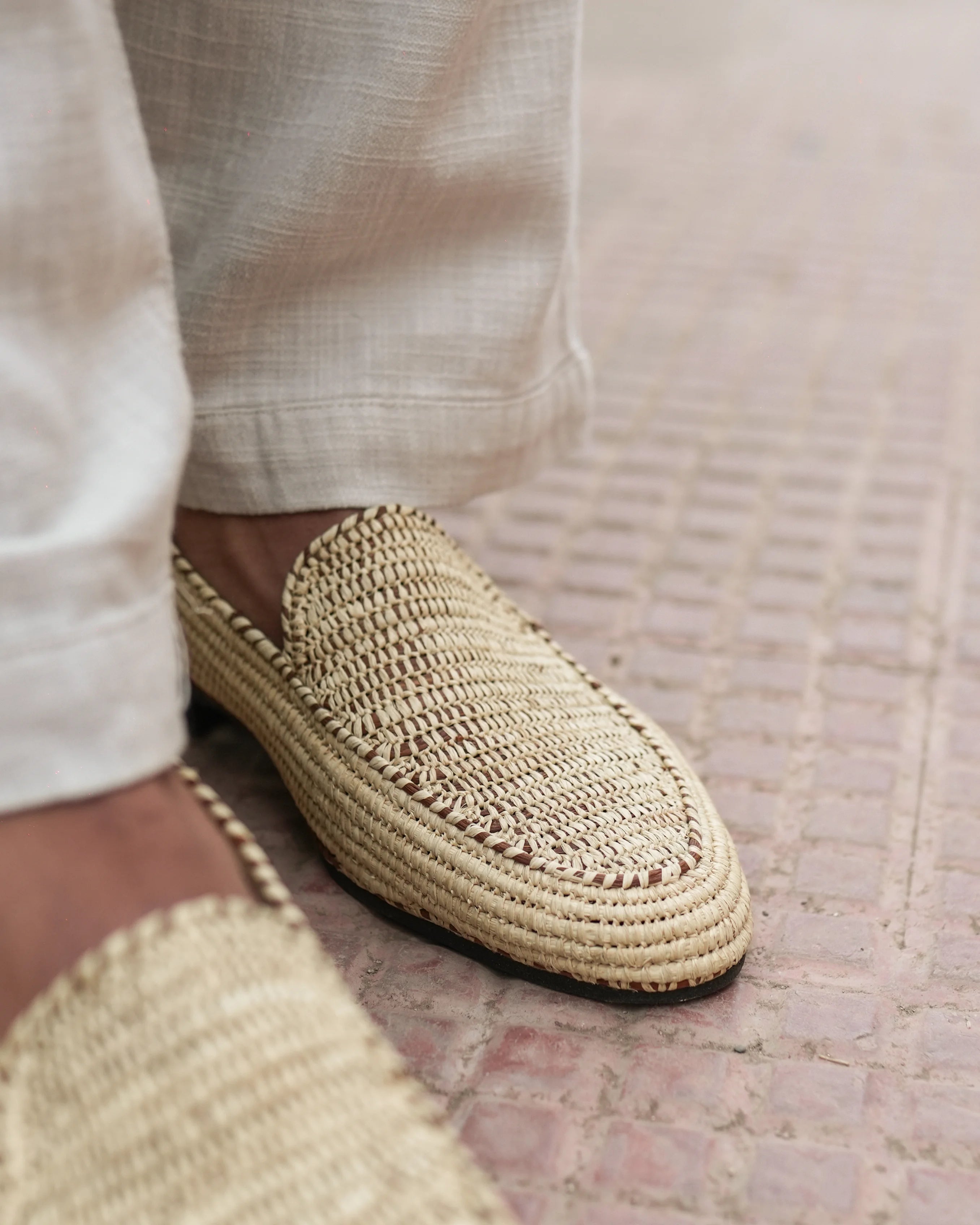 Close-up of a person wearing woven slippers on a textured floor.