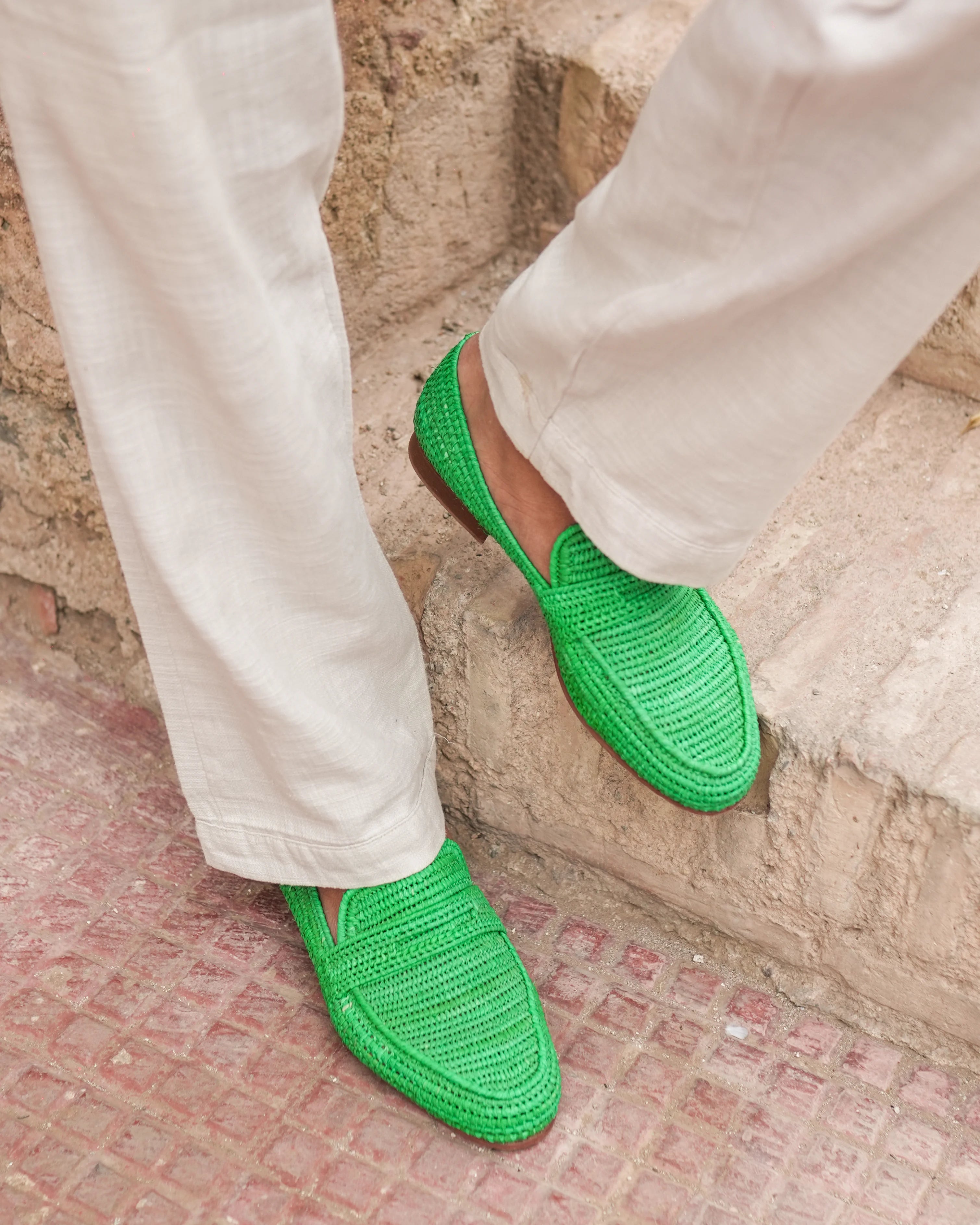 Green shoes worn with white pants on a stone pavement