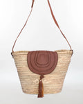 Woven basket bag with brown leather flap and tassel on a white background