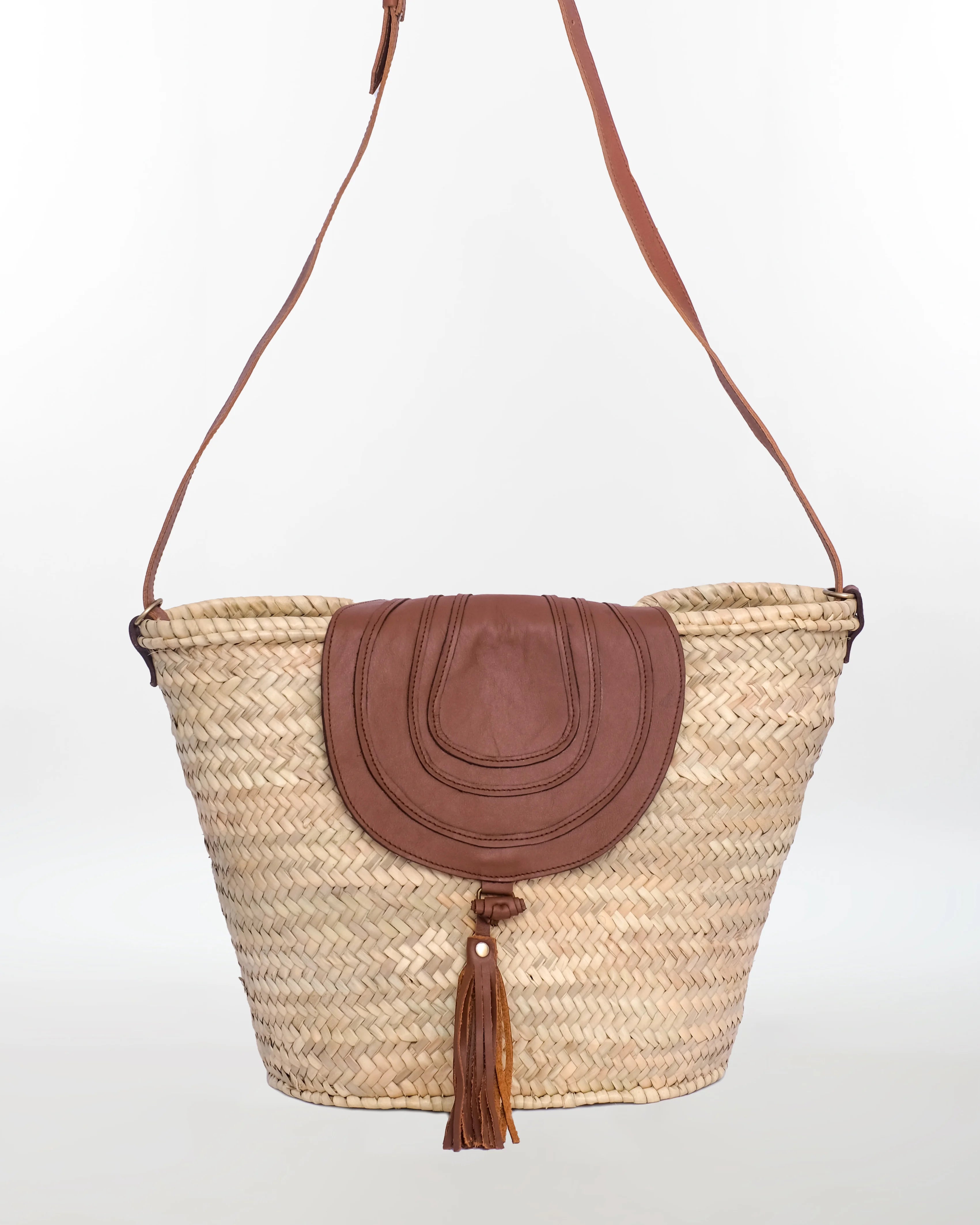 Woven basket bag with brown leather flap and tassel on a white background