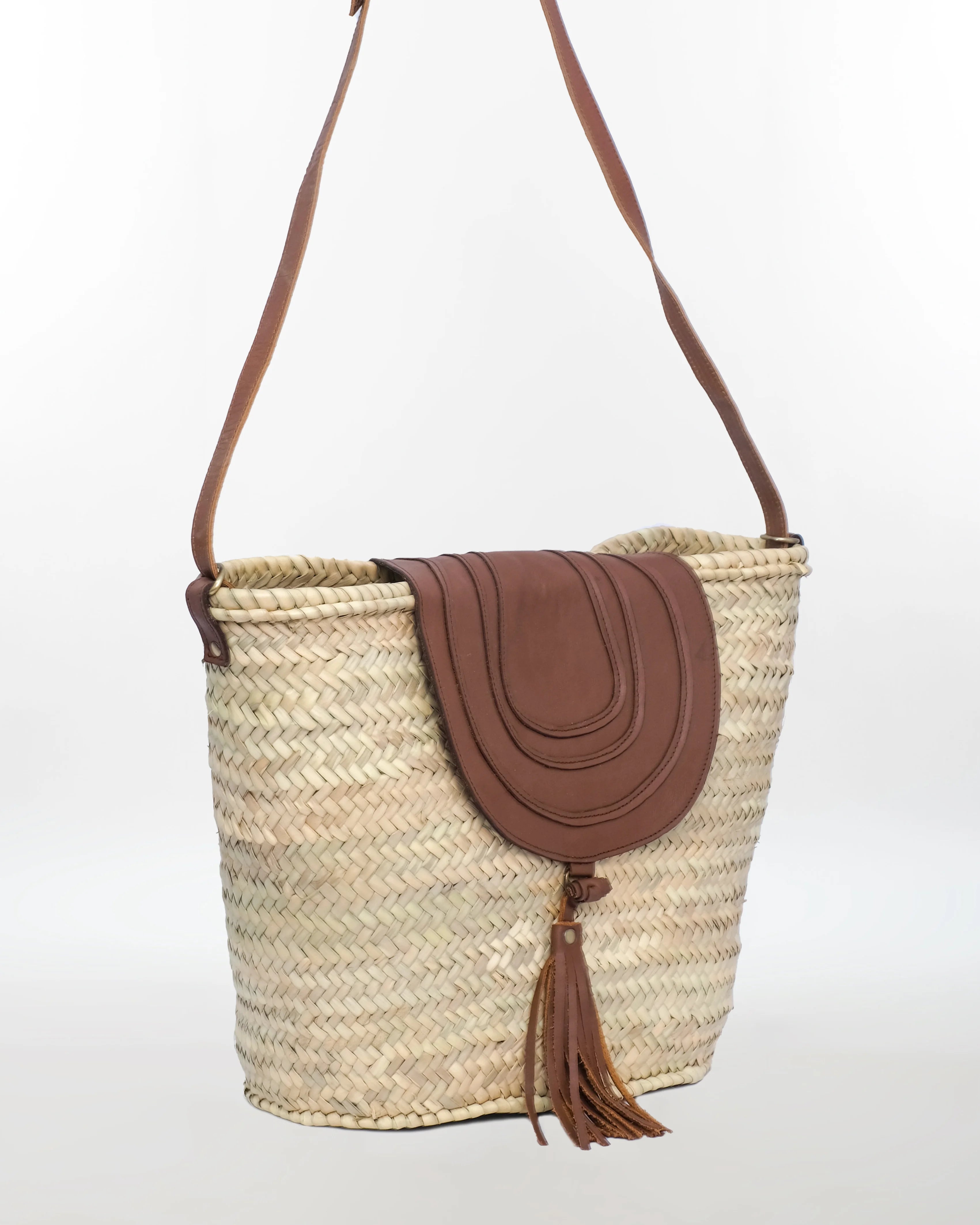 Woven basket bag with brown leather flap and tassel on a white background