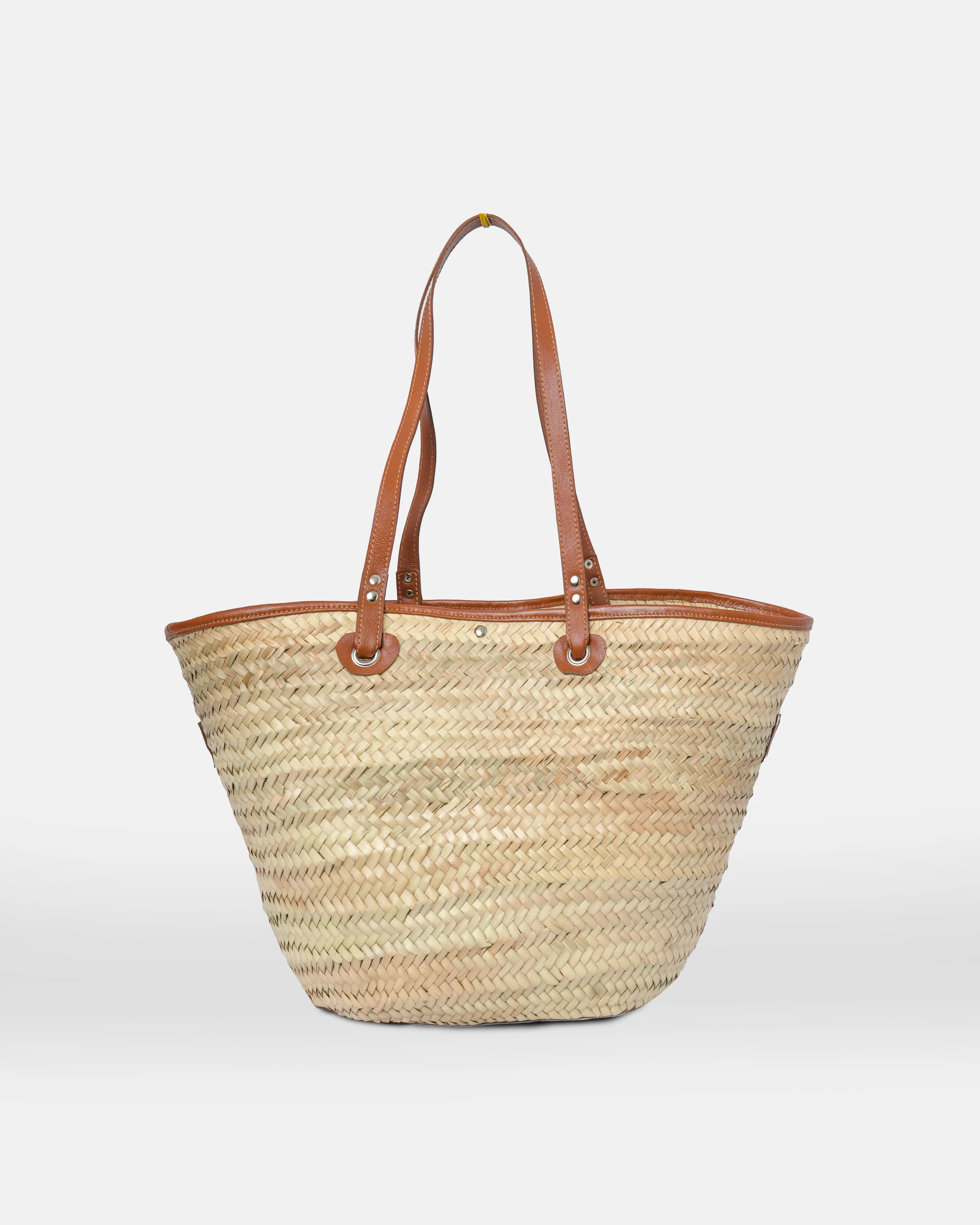 Woven straw tote bag with brown leather handles on a white background