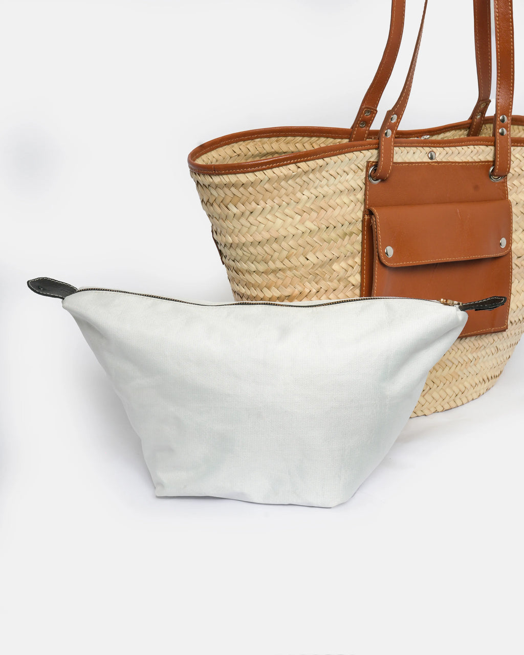 White tote bag and straw handbag with brown leather accents on a white background