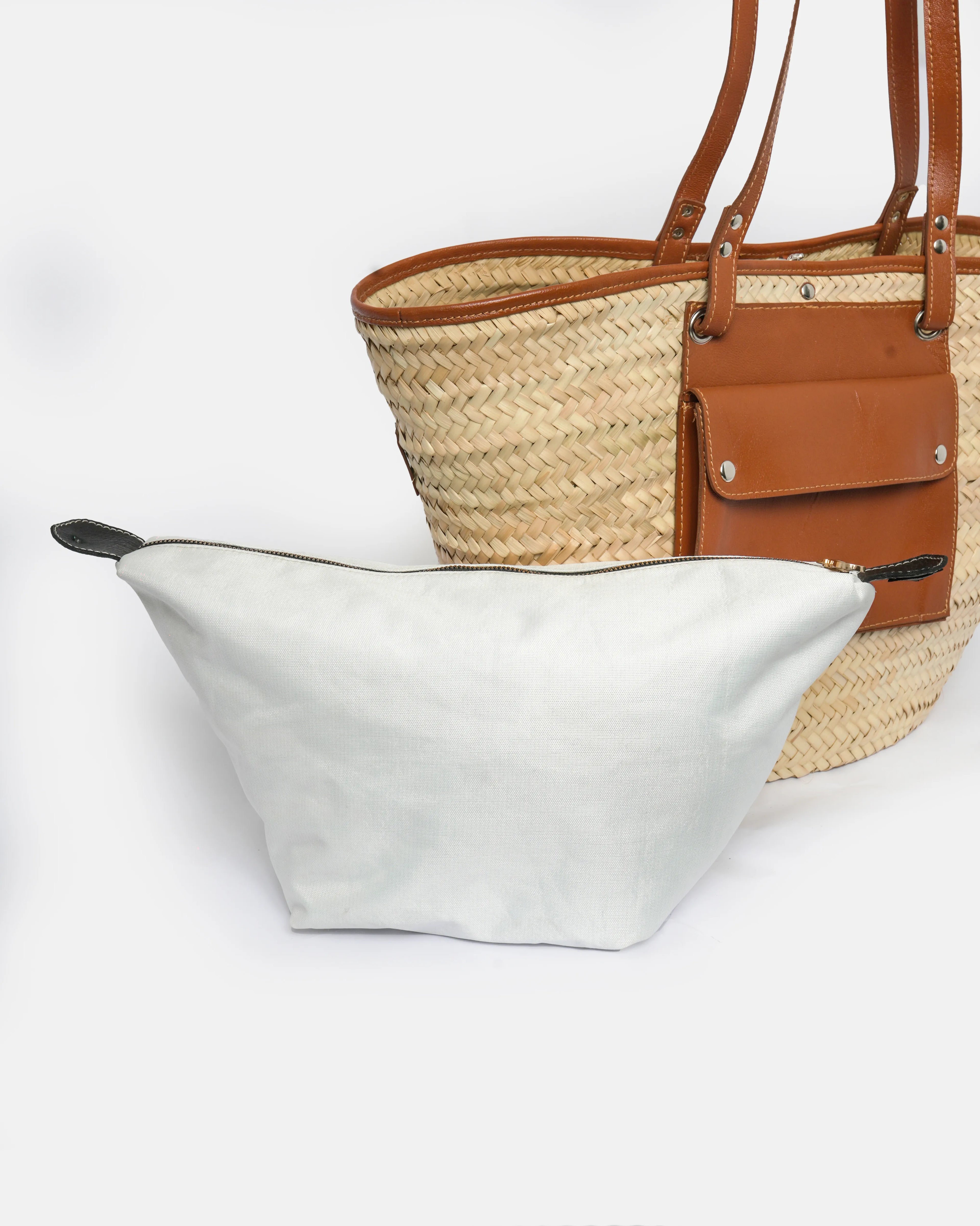 White tote bag and straw handbag with brown leather accents on a white background