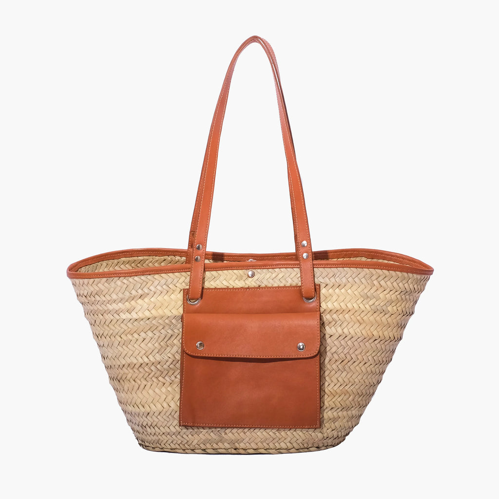 Woven straw tote bag with brown leather pocket and handle on a white background