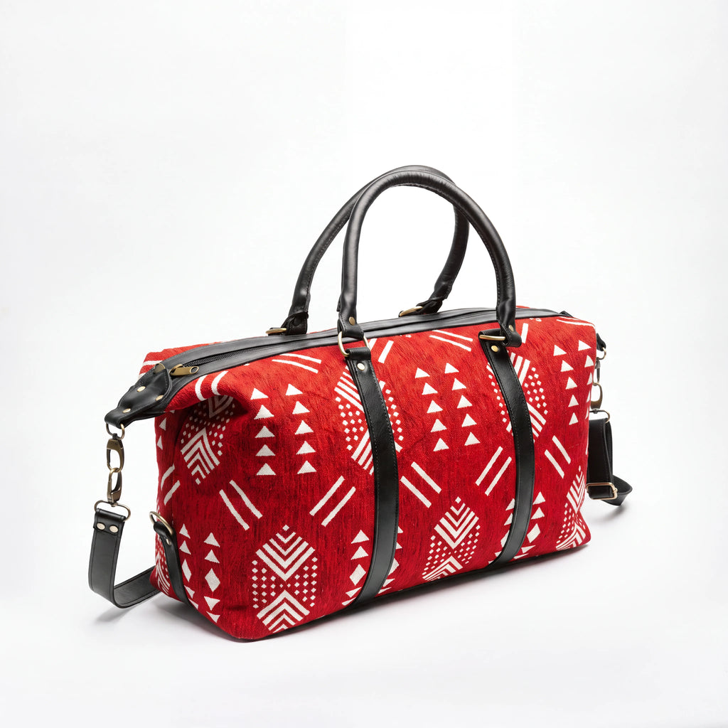 A red and white patterned duffel bag with black leather handles and straps, shown on a clean white background.