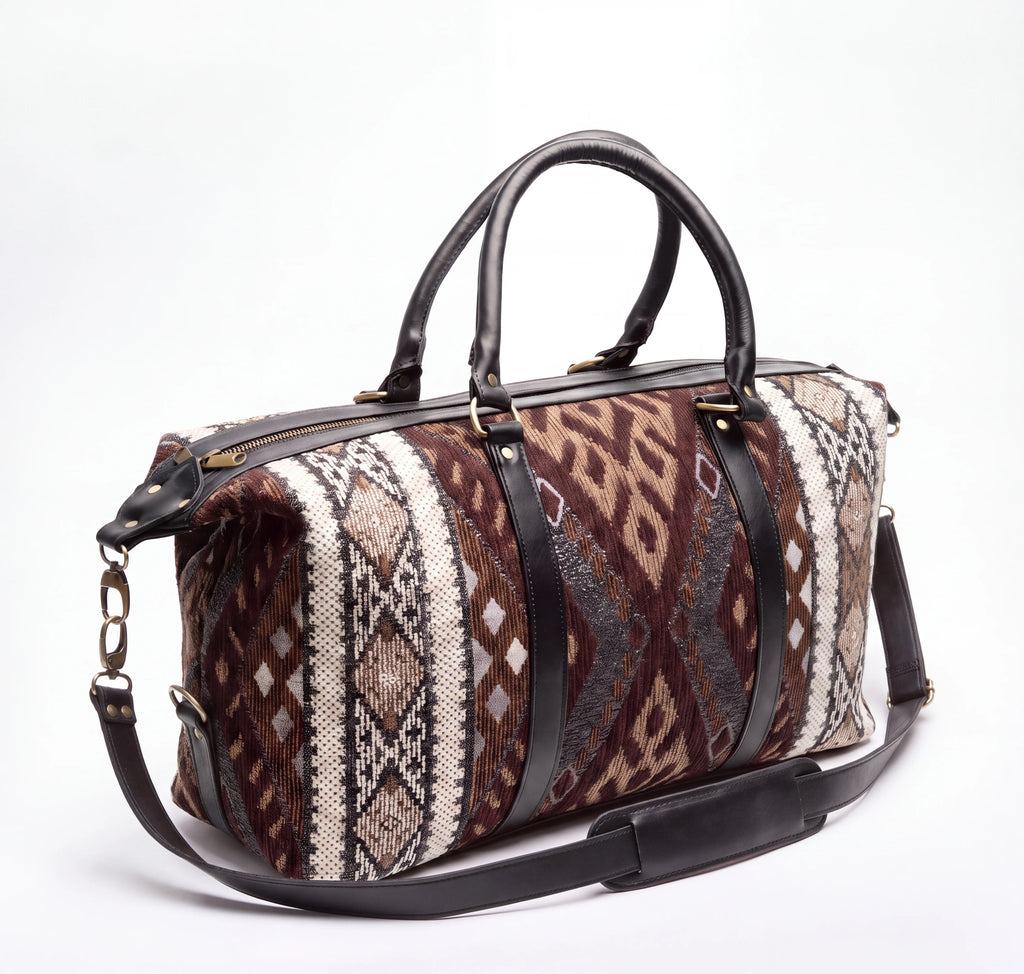 A duffel bag with a brown, beige, and gray geometric patterned fabric body, black leather handles and shoulder strap, and gold-tone hardware, photographed on a white background.