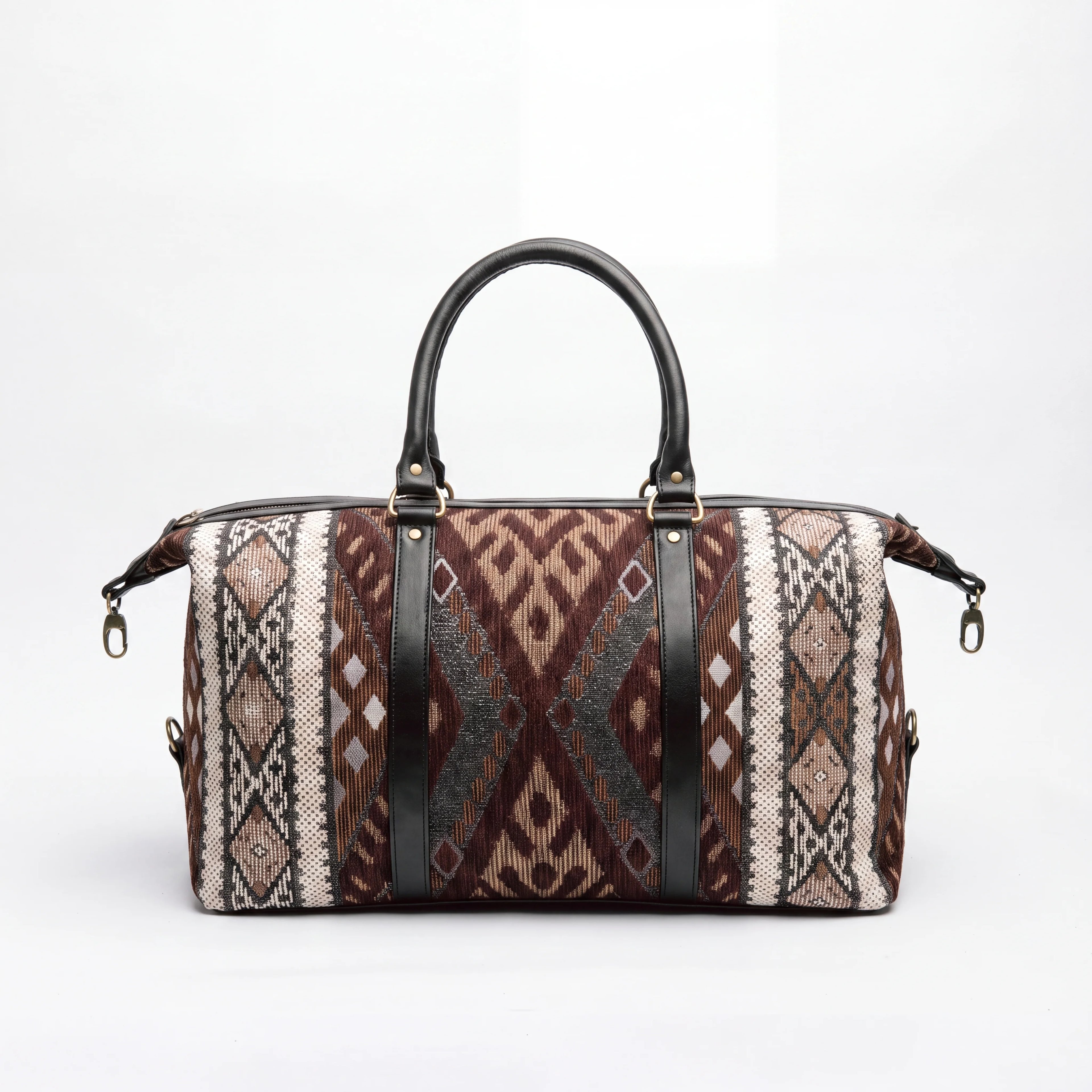 A duffle bag with a brown, beige, and black geometric patterned fabric body, featuring two black leather top handles and black vertical straps with gold-tone hardware, set against a plain white background.