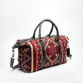 A duffel bag with a red, beige, and black geometric patterned fabric body, featuring black leather handles and trim, photographed on a white studio background.