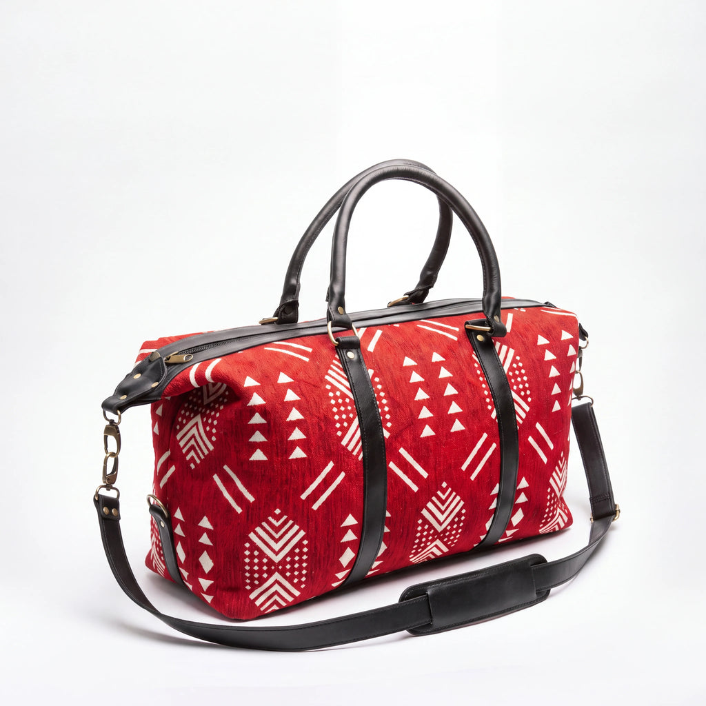 A red duffel bag with a white geometric tribal pattern and black leather handles and shoulder strap, shown on a white background.