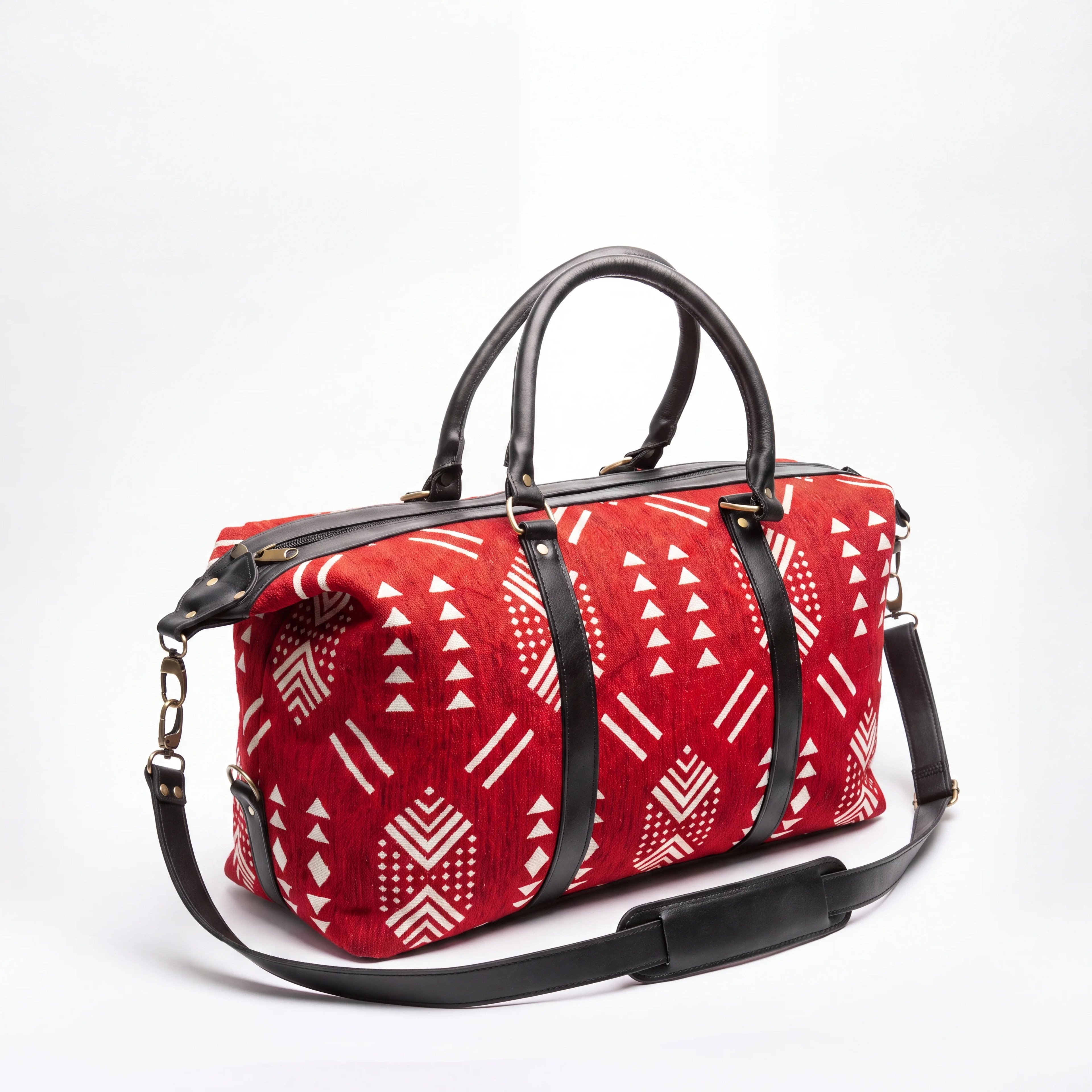 A red duffel bag with a white geometric tribal pattern and black leather handles and shoulder strap, shown on a white background.