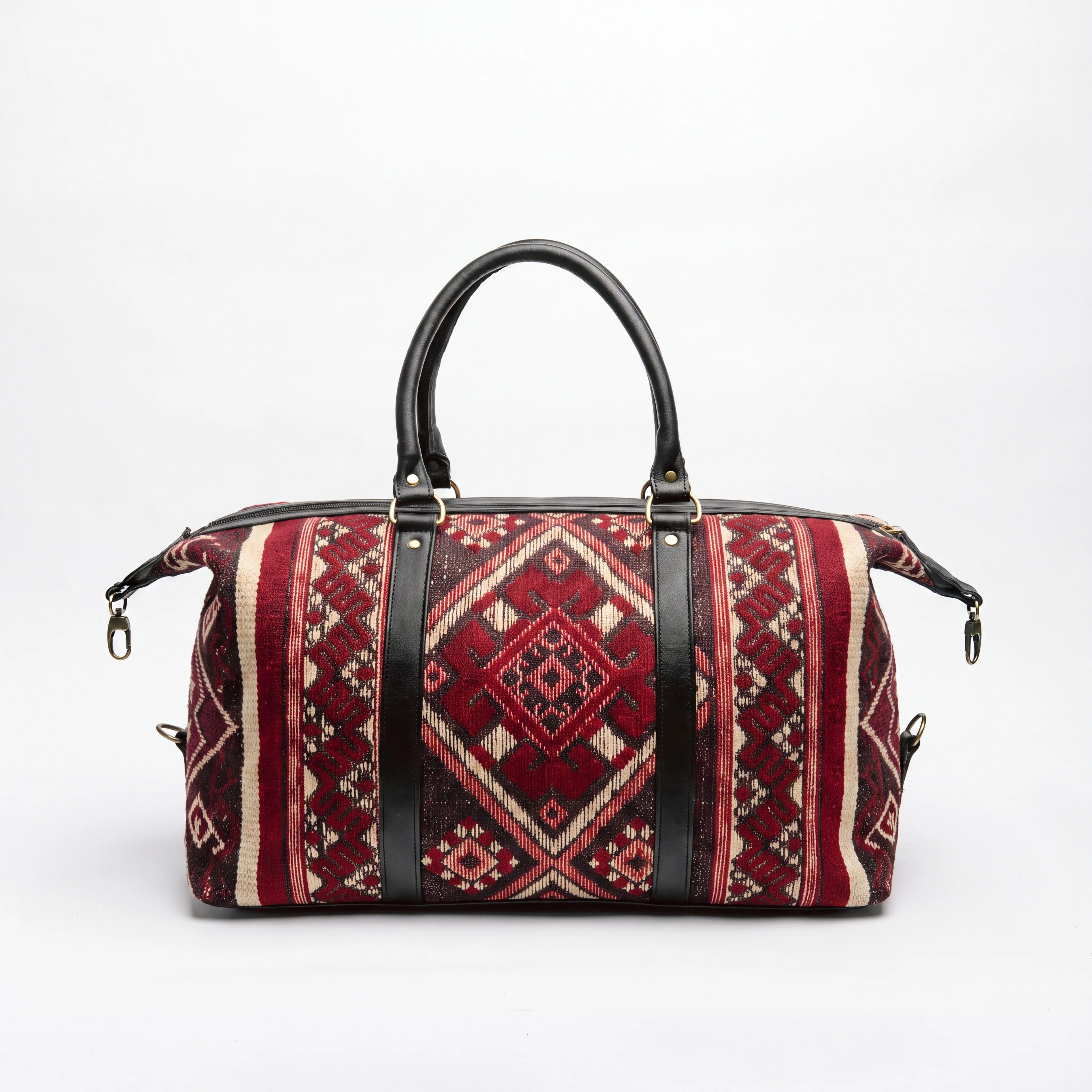A duffel bag with a red and beige geometric kilim pattern and black leather handles and straps, shown on a white background.