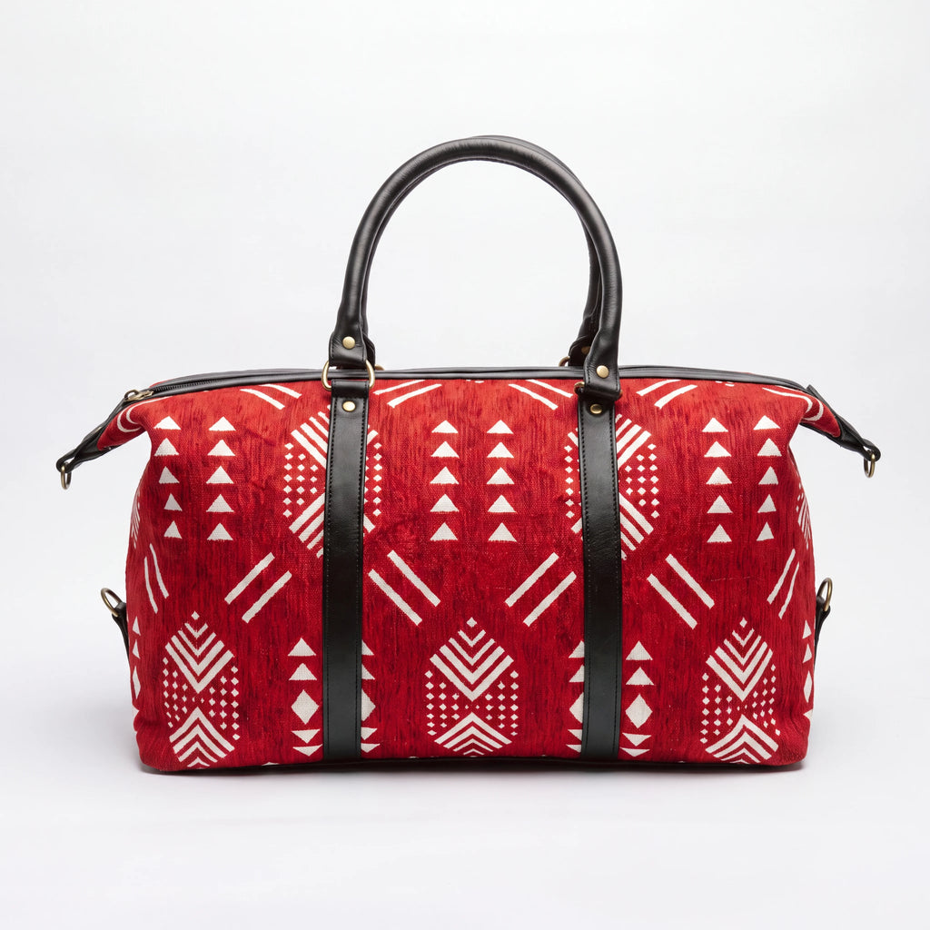 A red duffle bag with a white geometric tribal pattern and black leather handles and straps, shown against a plain white background.