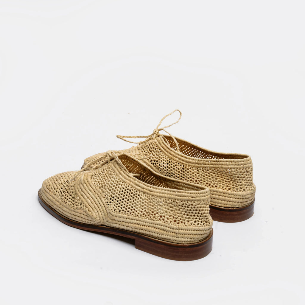 A pair of woven straw lace-up shoes with dark brown soles, photographed on a clean white background.