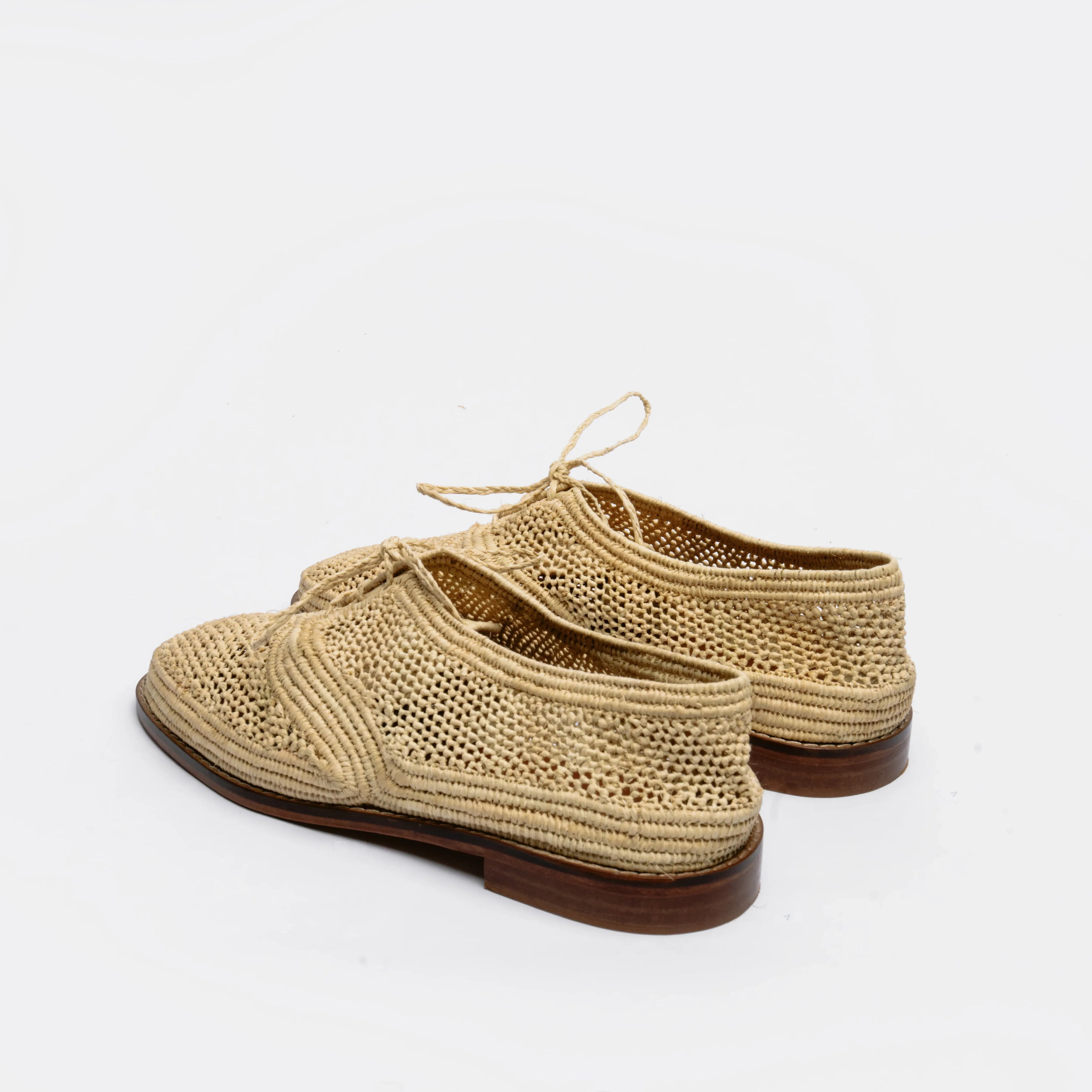 A pair of woven straw lace-up shoes with dark brown soles, photographed on a clean white background.