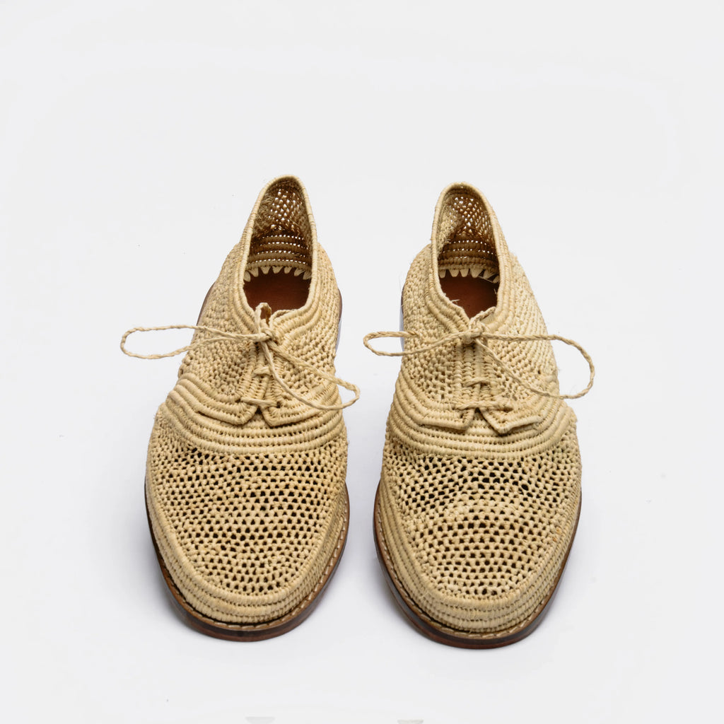 A pair of woven straw lace-up shoes with a textured openwork pattern and brown soles, photographed on a clean white background.