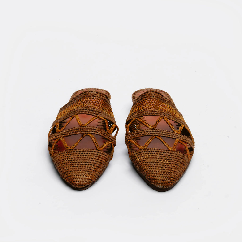 A pair of brown woven raffia mule sandals with criss-cross woven straps, shown on a plain white background.