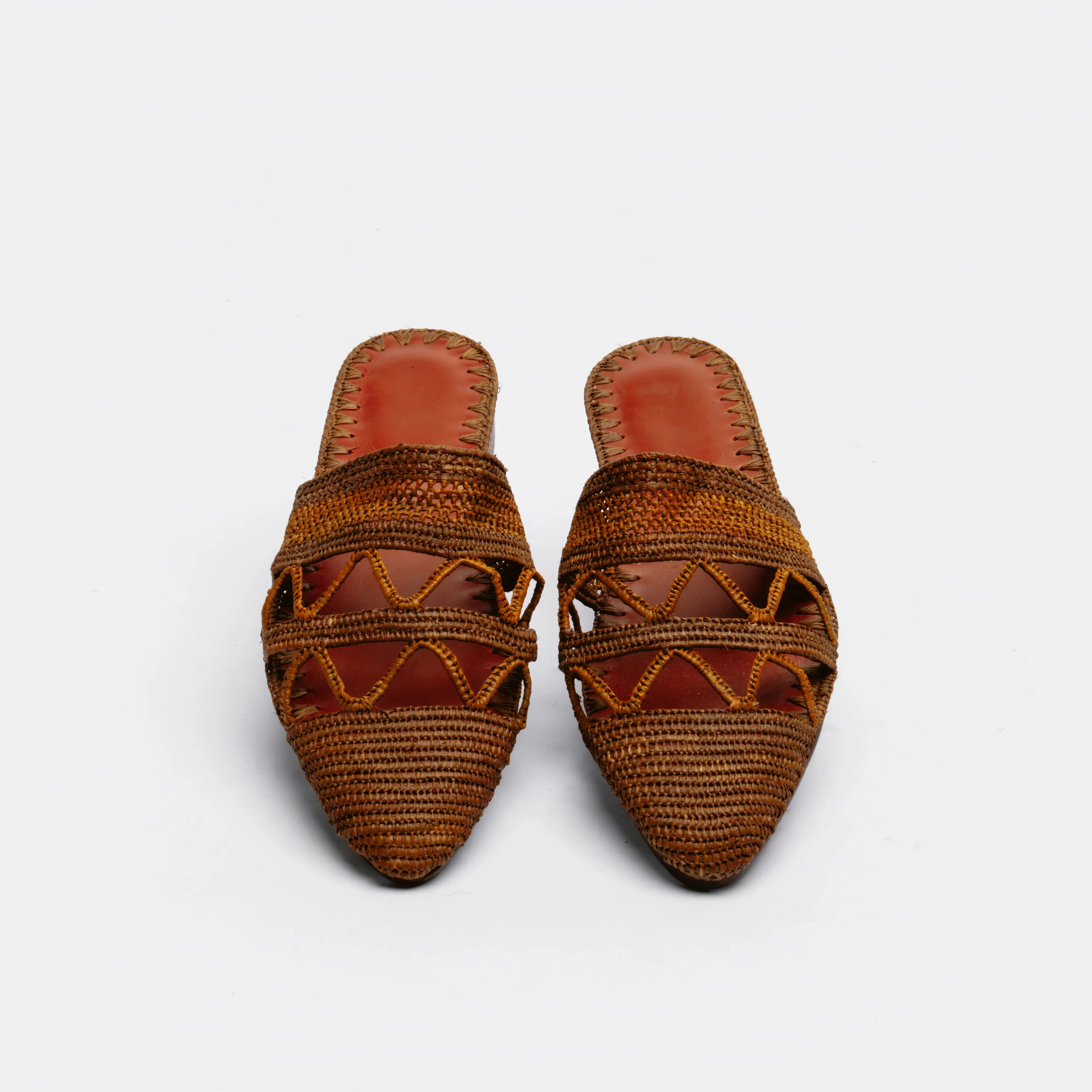 A pair of brown woven raffia mule sandals with geometric cutout patterns and pointed toes, shown on a light gray background.