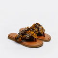 A pair of thong sandals with tan leather footbeds and straps adorned with textured, ruffled dried flowers in mustard yellow, brown, and beige, set against a plain white background.