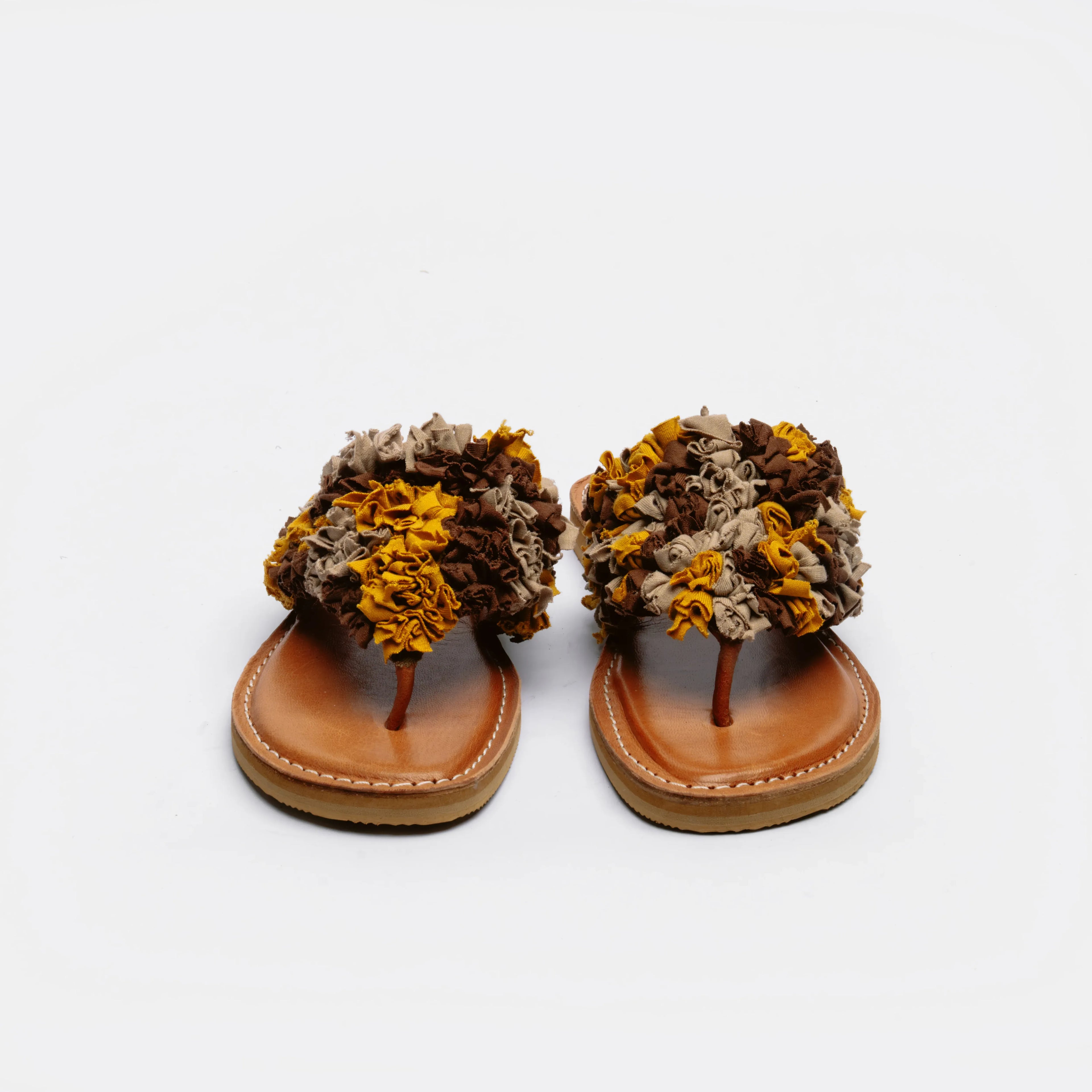A pair of thong sandals with chunky, textured floral straps in brown, beige, and mustard yellow, set on tan leather footbeds against a plain white background.