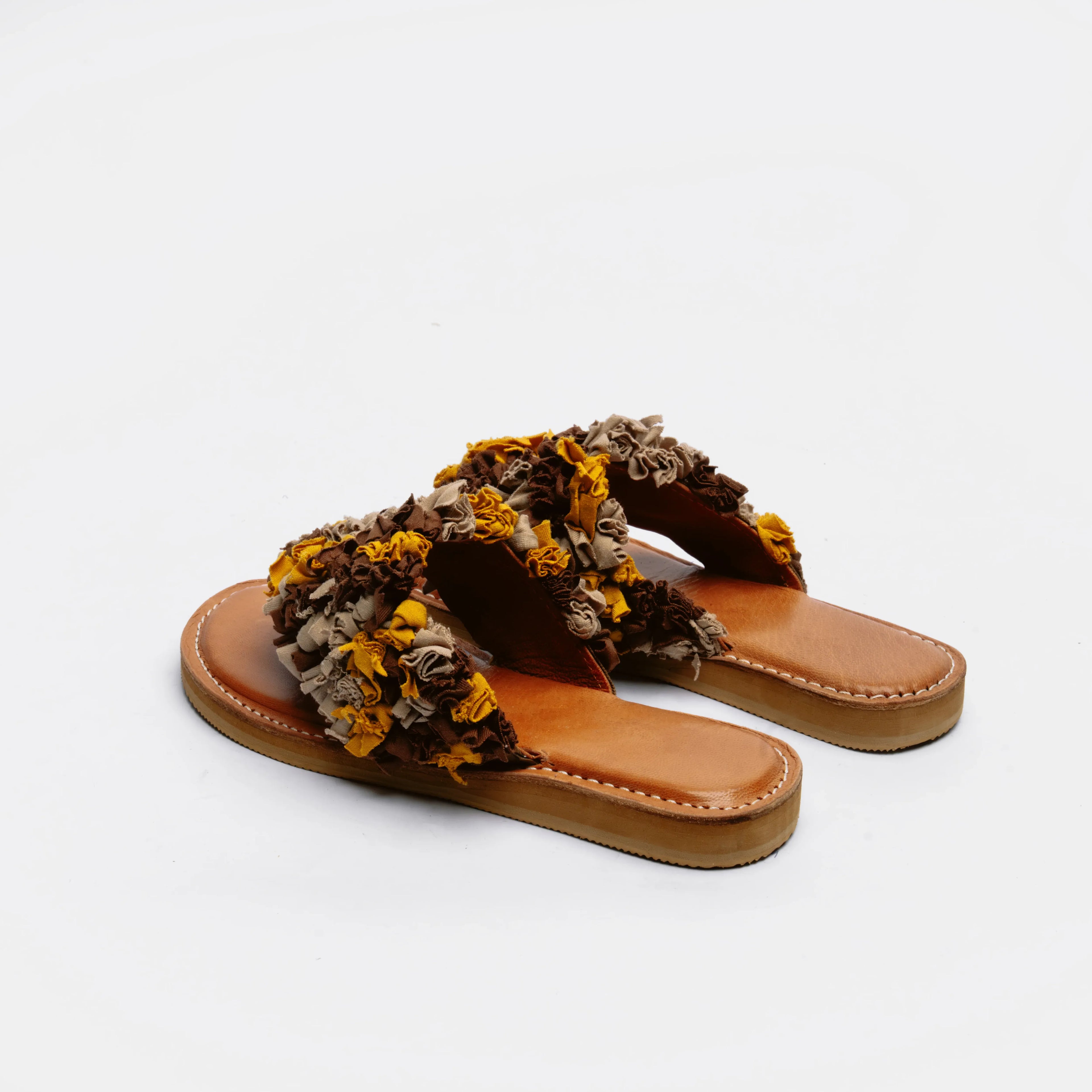 A pair of women's flat slide sandals with wide, textured ruffled straps in brown, beige, and mustard yellow, set against a plain white background.