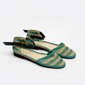 A pair of woven flat sandals with green and beige horizontal stripes, black ankle straps with gold-tone buckles, and a low black heel, shown on a white background.