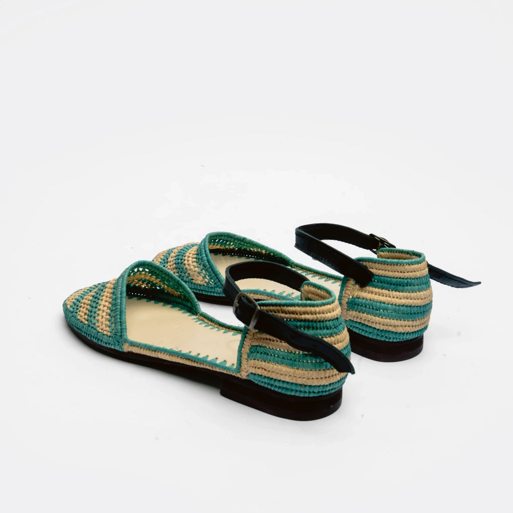 A pair of woven flat sandals with teal green and beige stripes, black straps, and black soles, photographed on a clean white background.