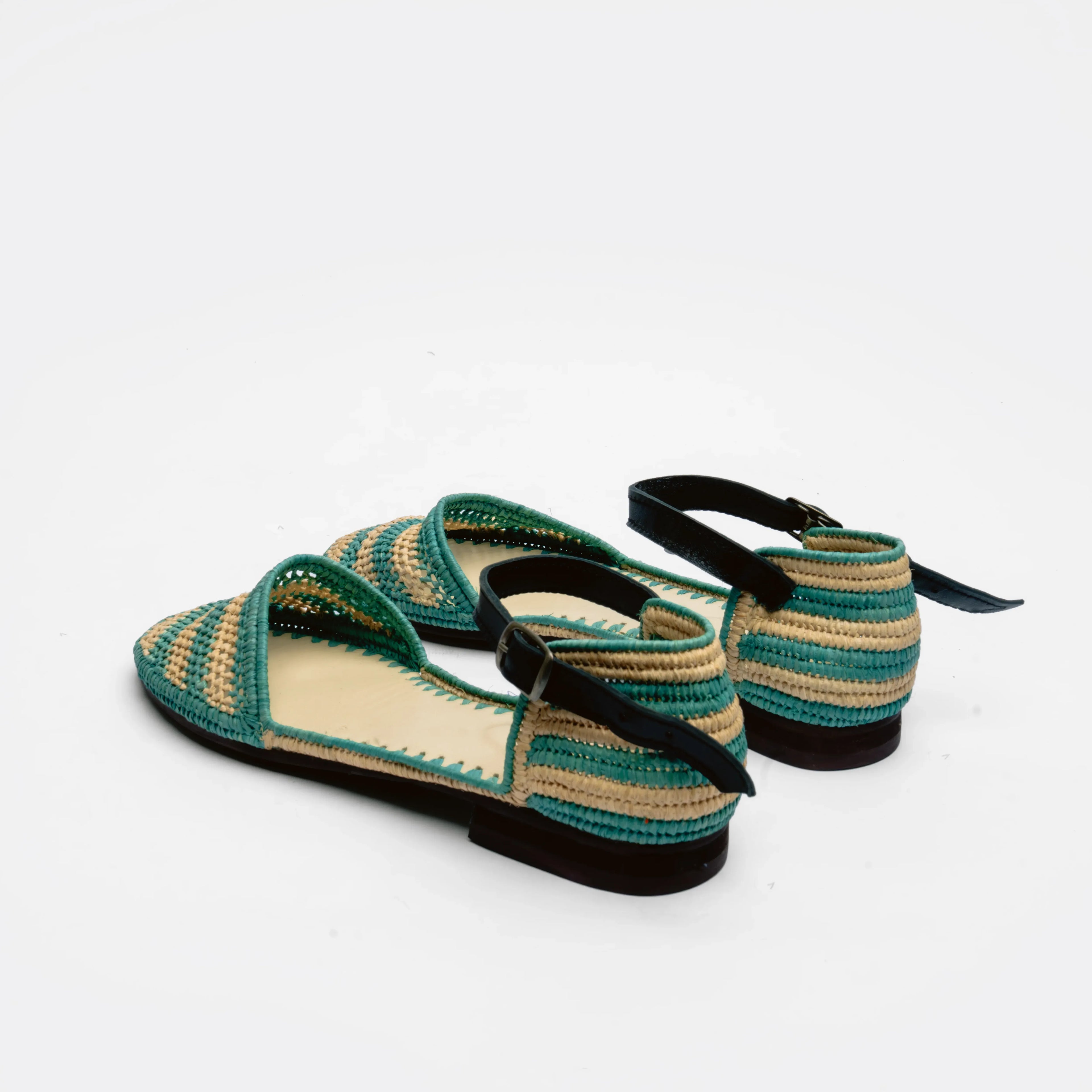 A pair of woven flat sandals with teal green and beige stripes, black straps, and black soles, photographed on a clean white background.