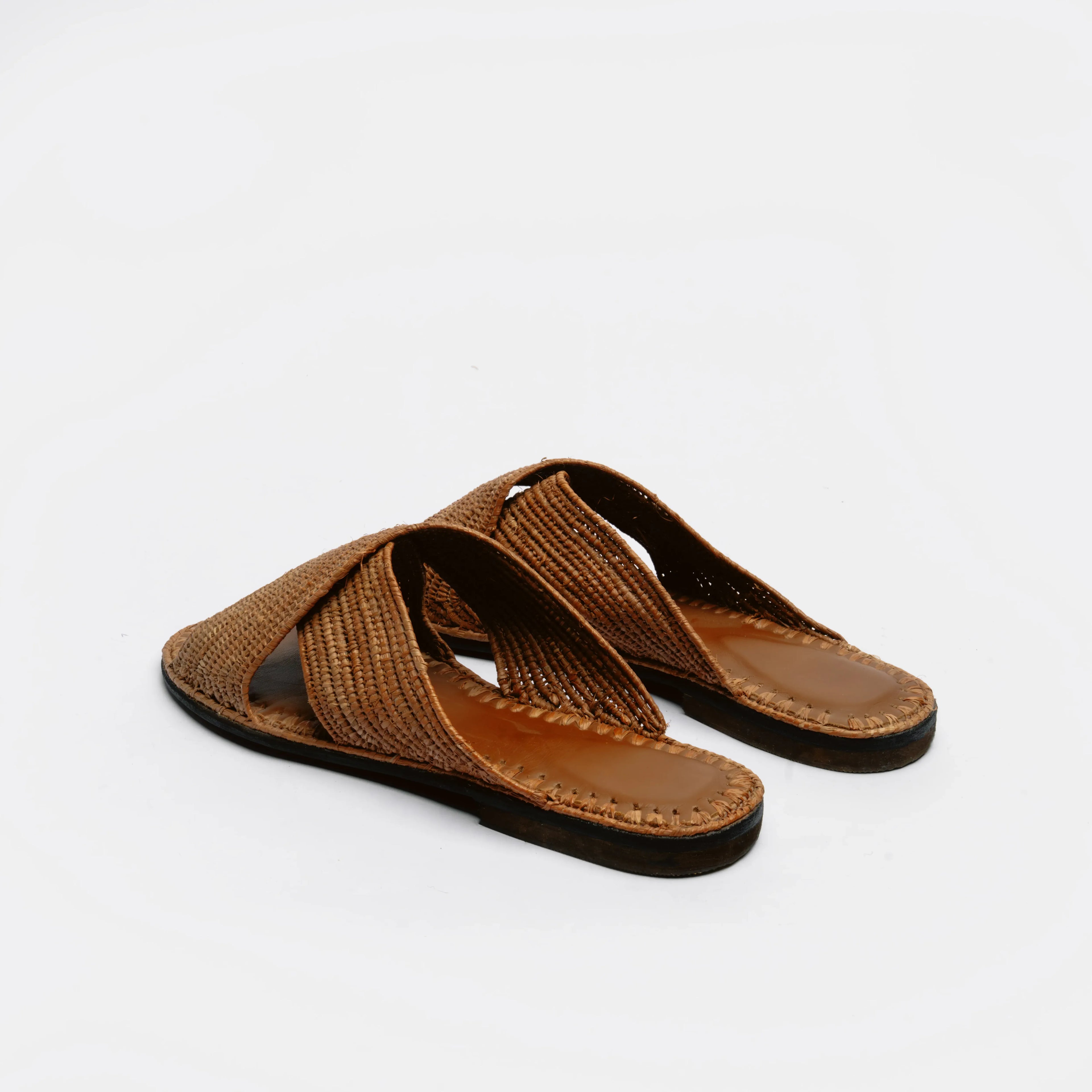 A pair of brown woven slide sandals with flat soles, shown from a three-quarters angle on a plain white background.