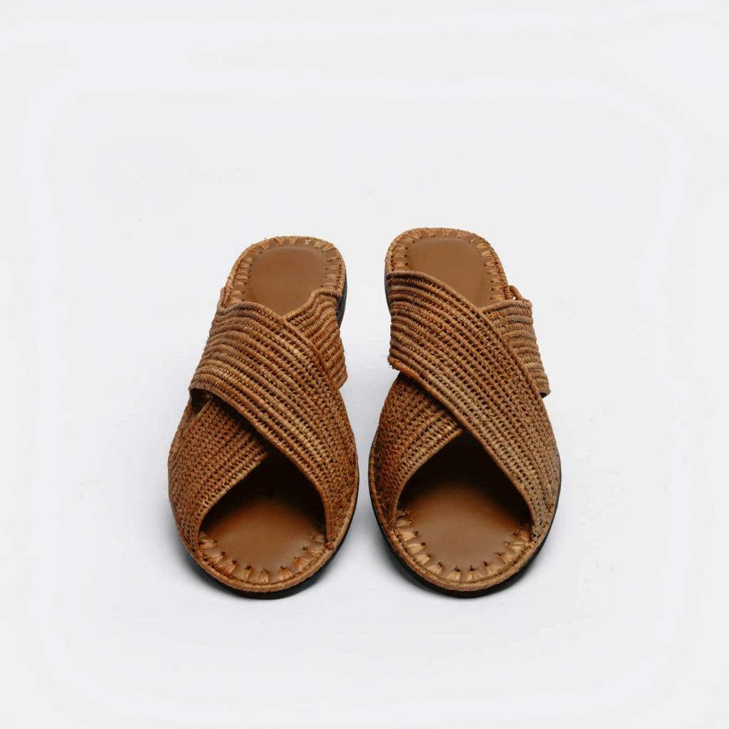 A pair of brown woven leather slide sandals with crisscross straps, shown from a top-down view on a light gray background.