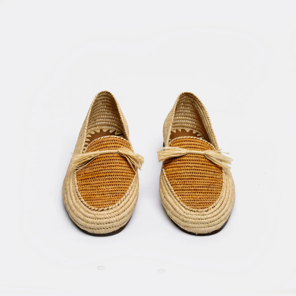 A pair of woven raffia espadrille-style loafers with tan crochet detailing and small tassel accents on the vamp, photographed against a clean white background.