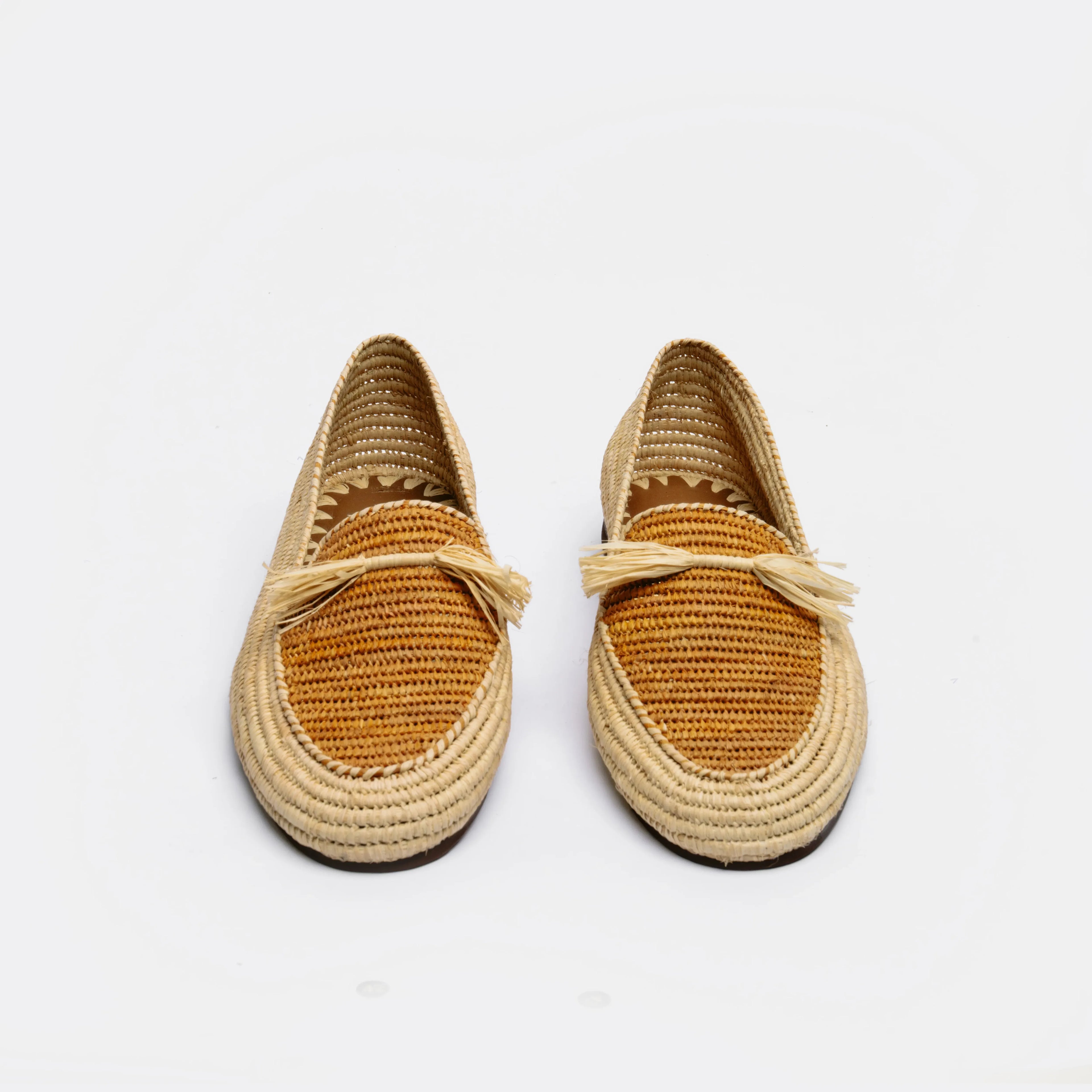 A pair of woven raffia espadrille-style loafers with tan crochet detailing and small tassel accents on the vamp, photographed against a clean white background.