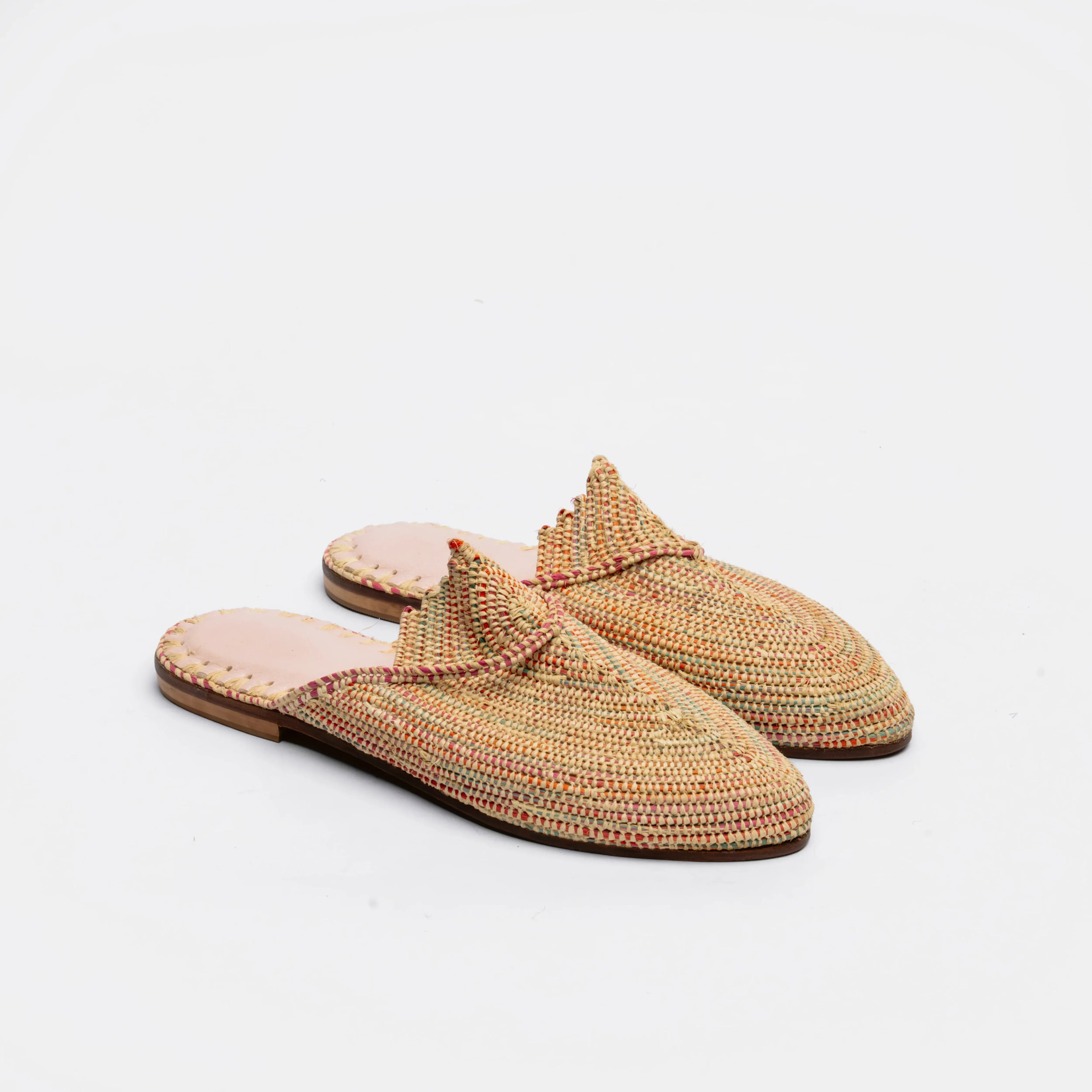 A pair of woven slip-on mule sandals with a textured multicolor pattern of beige, orange, and green threads, featuring a light pink insole and a dark brown outsole, set against a plain white background.
