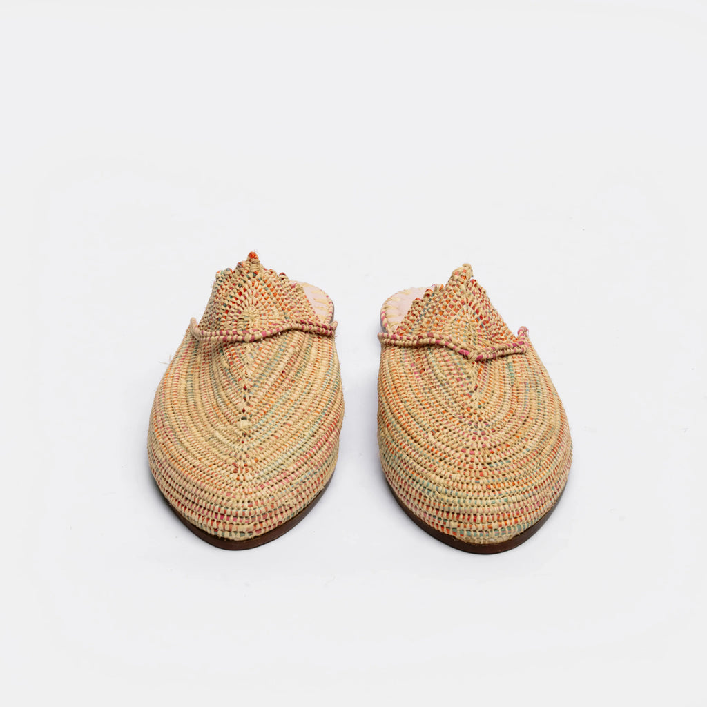 A pair of handmade woven mule slippers in a multicolor spiral pattern of beige, orange, green, and red, shown from a top-down view on a white background.