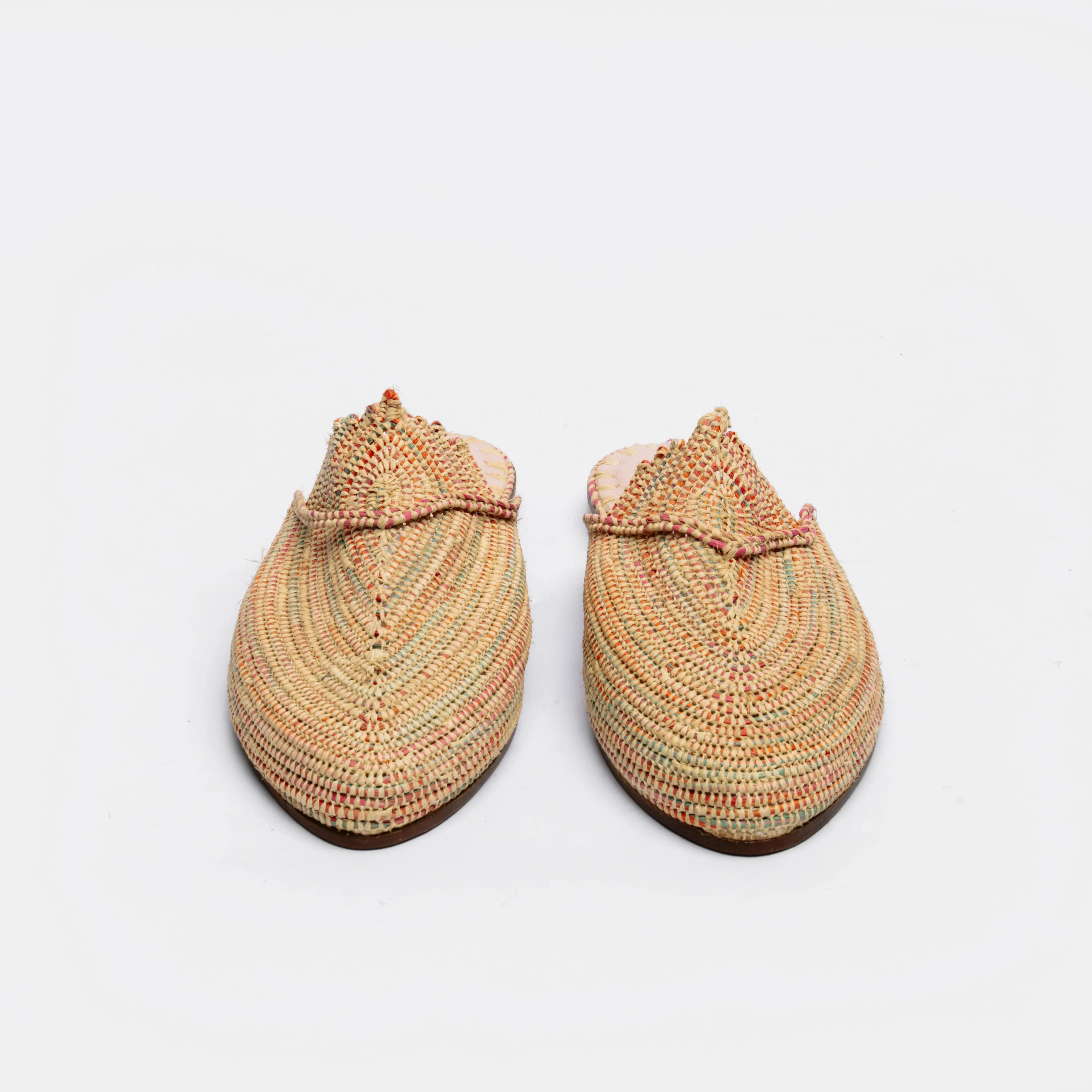A pair of handmade woven mule slippers in a multicolor spiral pattern of beige, orange, green, and red, shown from a top-down view on a white background.