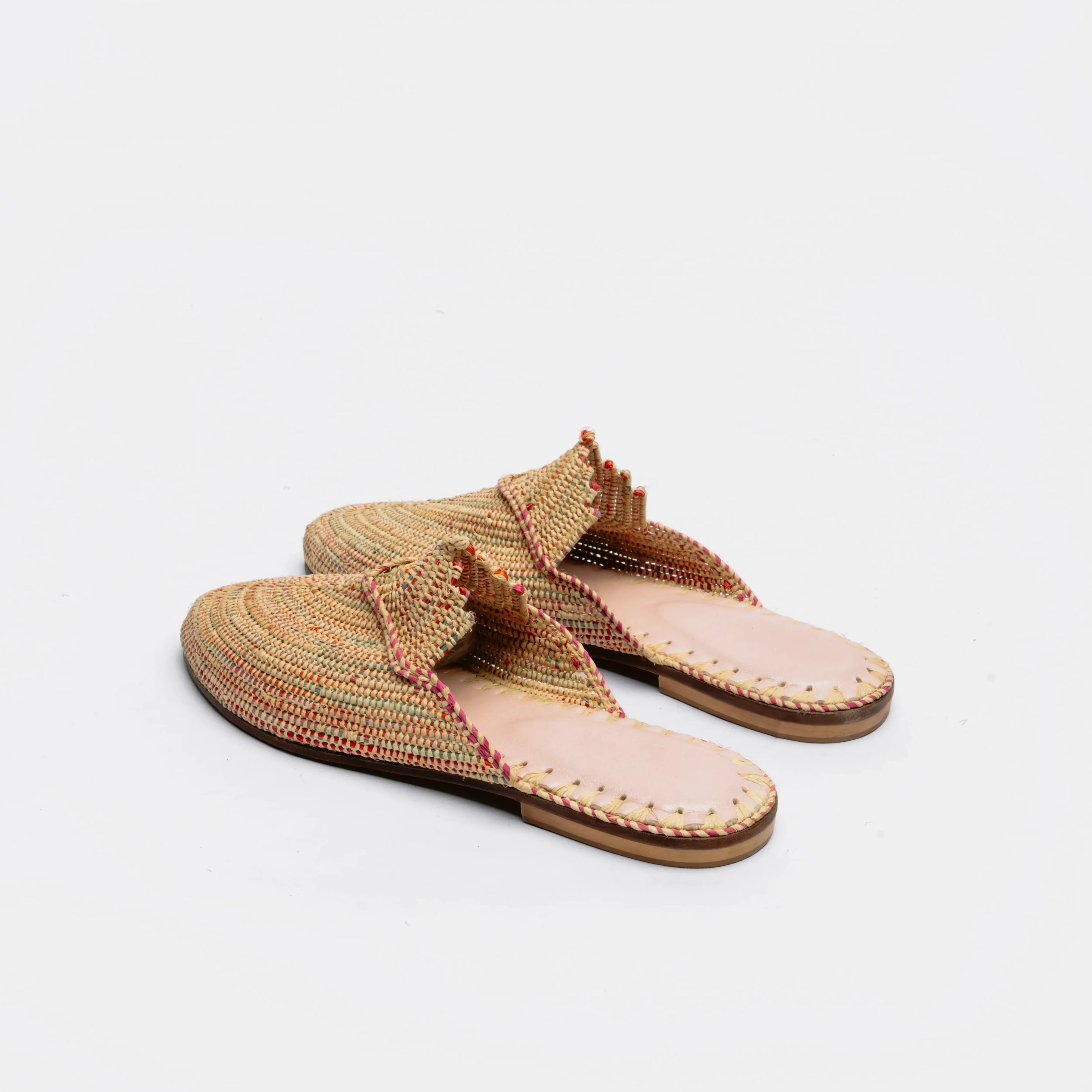 A pair of woven thong-style mule sandals in a multicolor tan, beige, and brown pattern with a light pink footbed and brown soles, photographed on a clean white background.