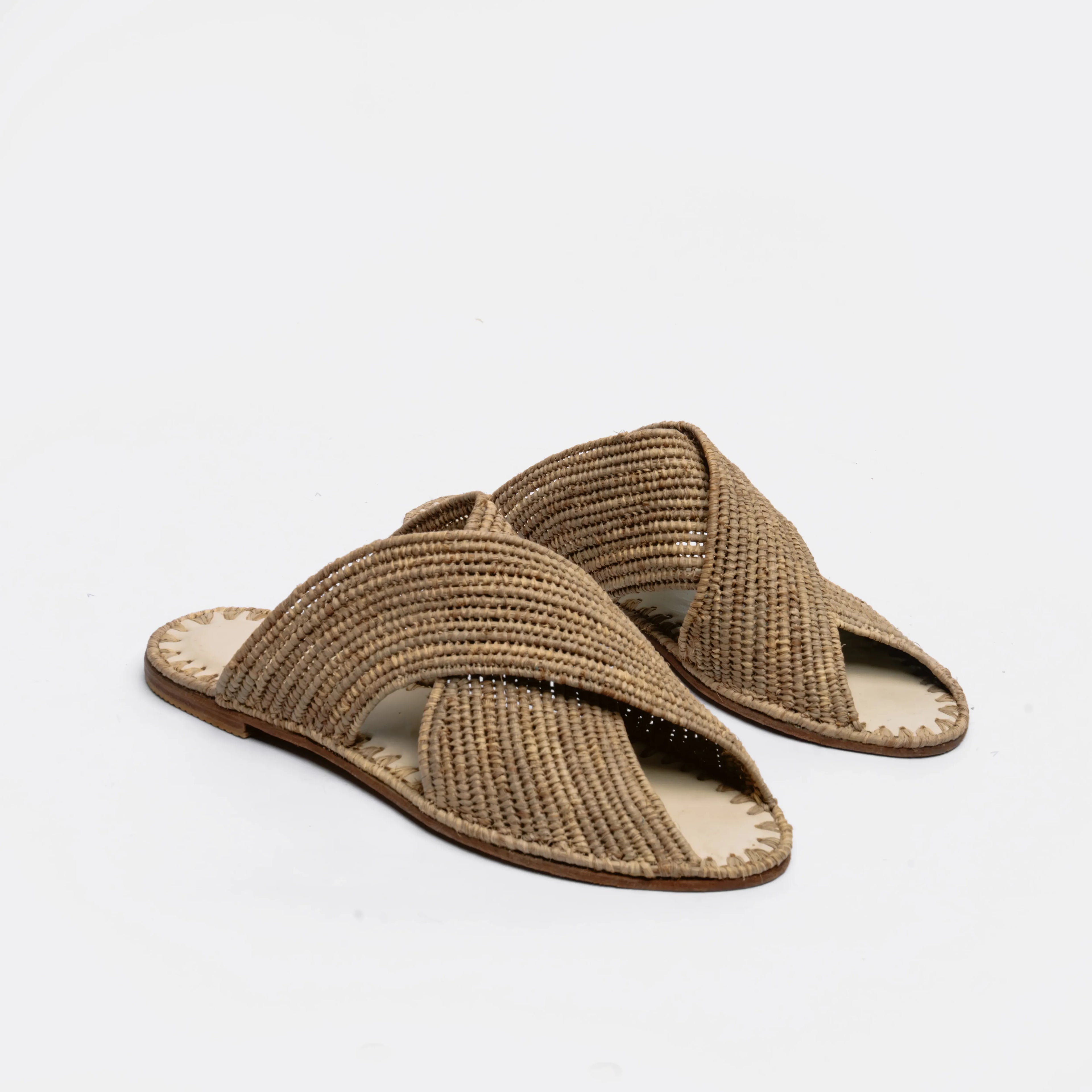 A pair of woven straw slide sandals with crisscrossing straps, shown on a clean white background.