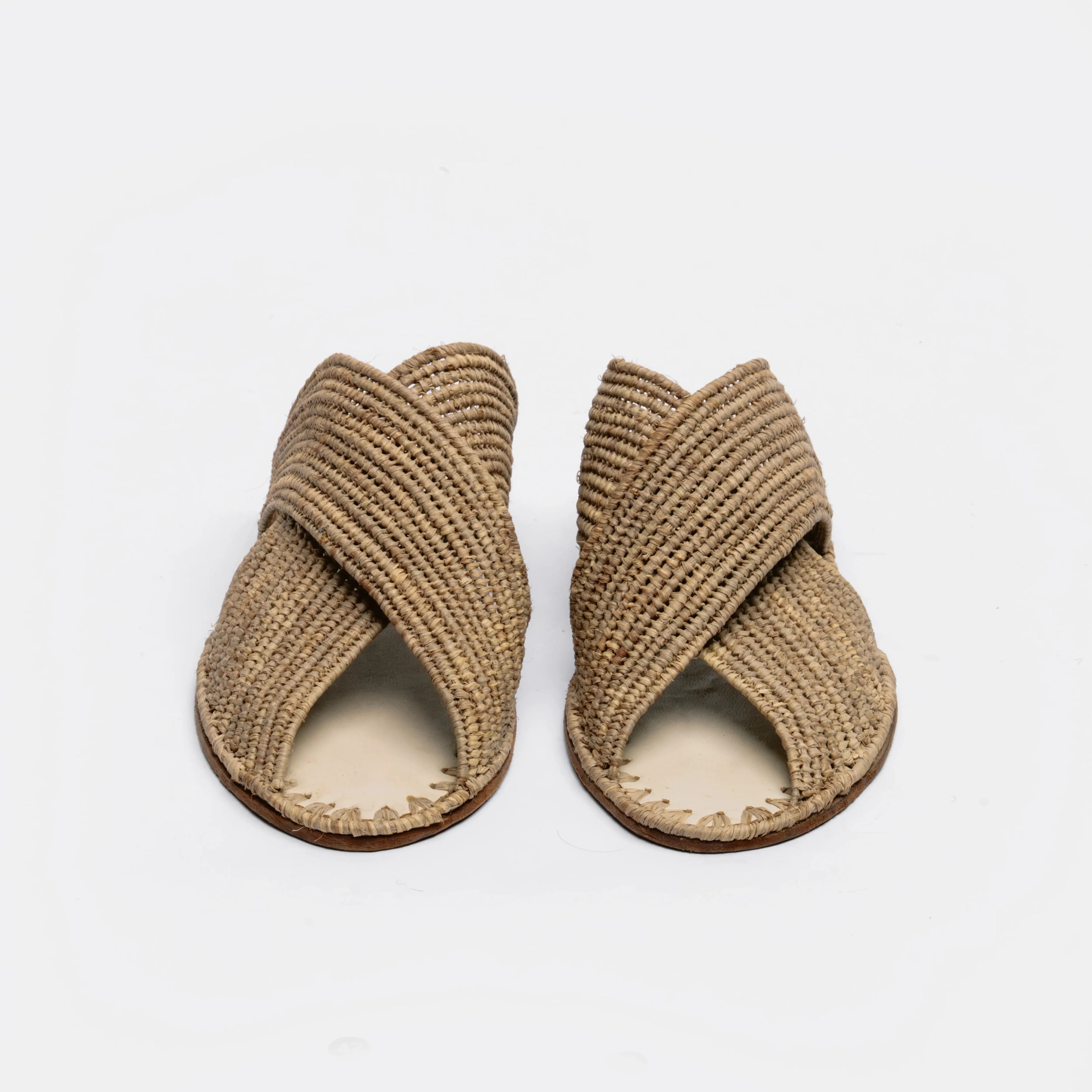 A pair of woven straw slide sandals with crisscrossing straps, shown from a top-down view on a clean white background.