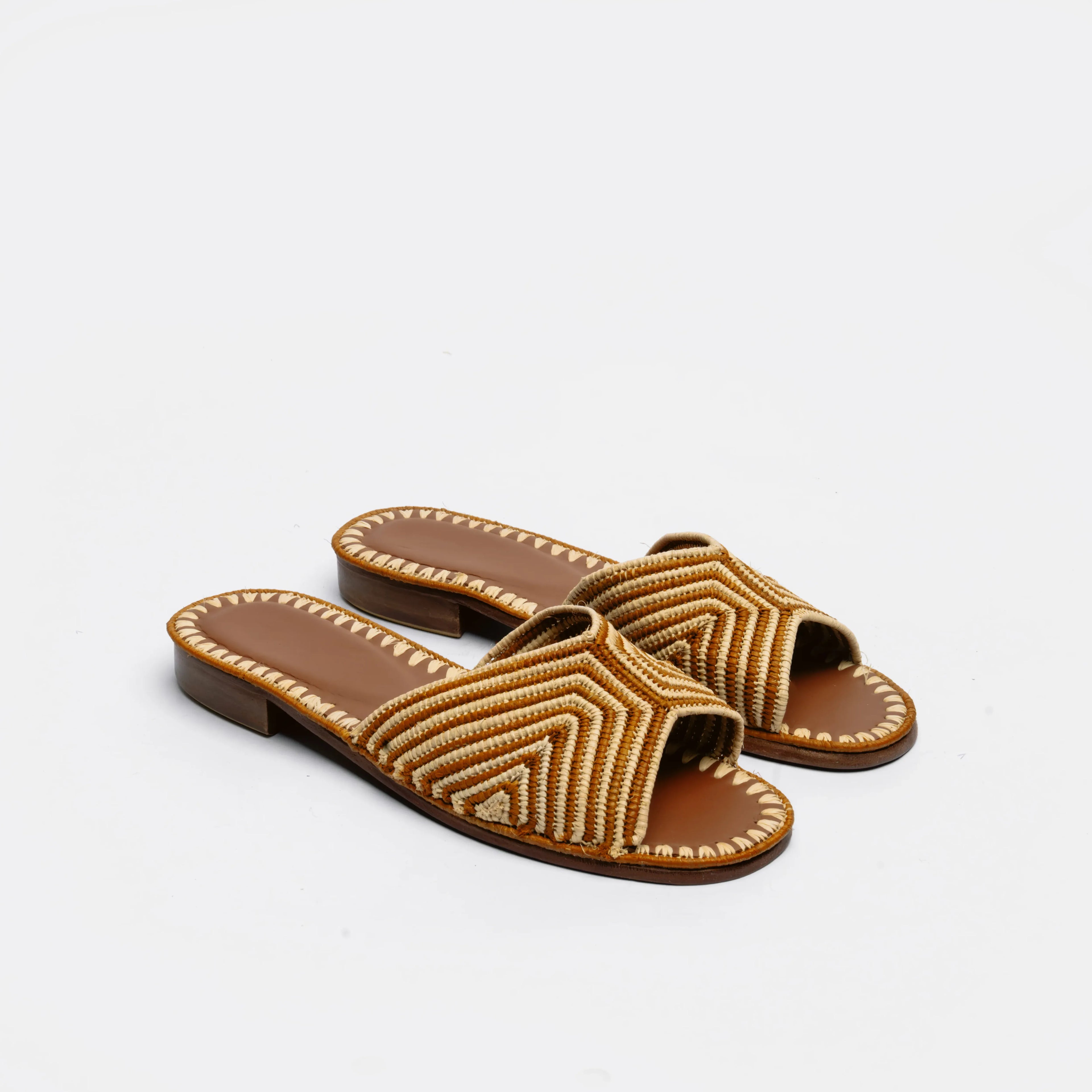 A pair of women's open-toe slide sandals with brown leather straps featuring a beige woven geometric chevron pattern, set against a plain light gray background.