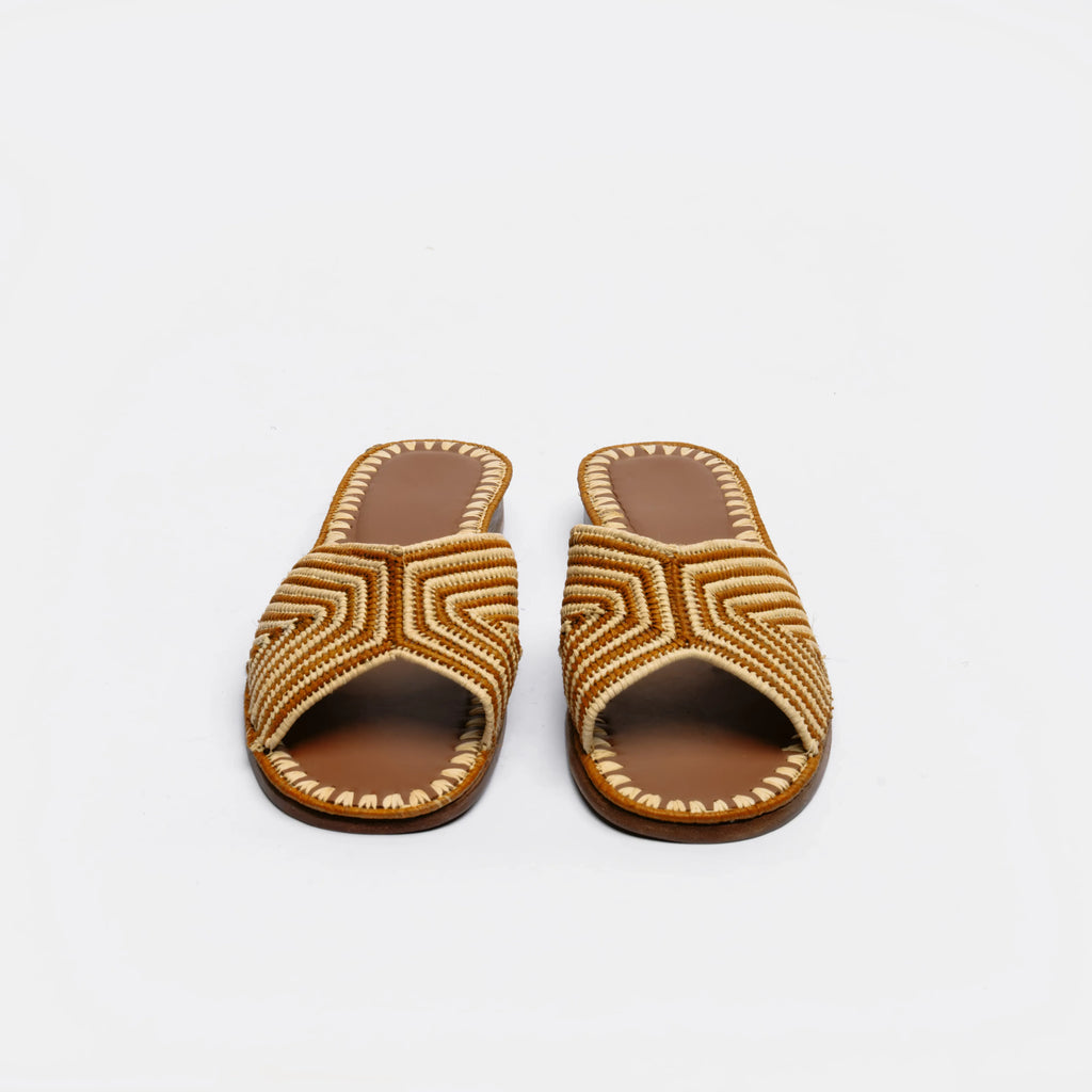 A pair of open-toe slide sandals with geometric braided straps in brown and beige, set against a plain white background.