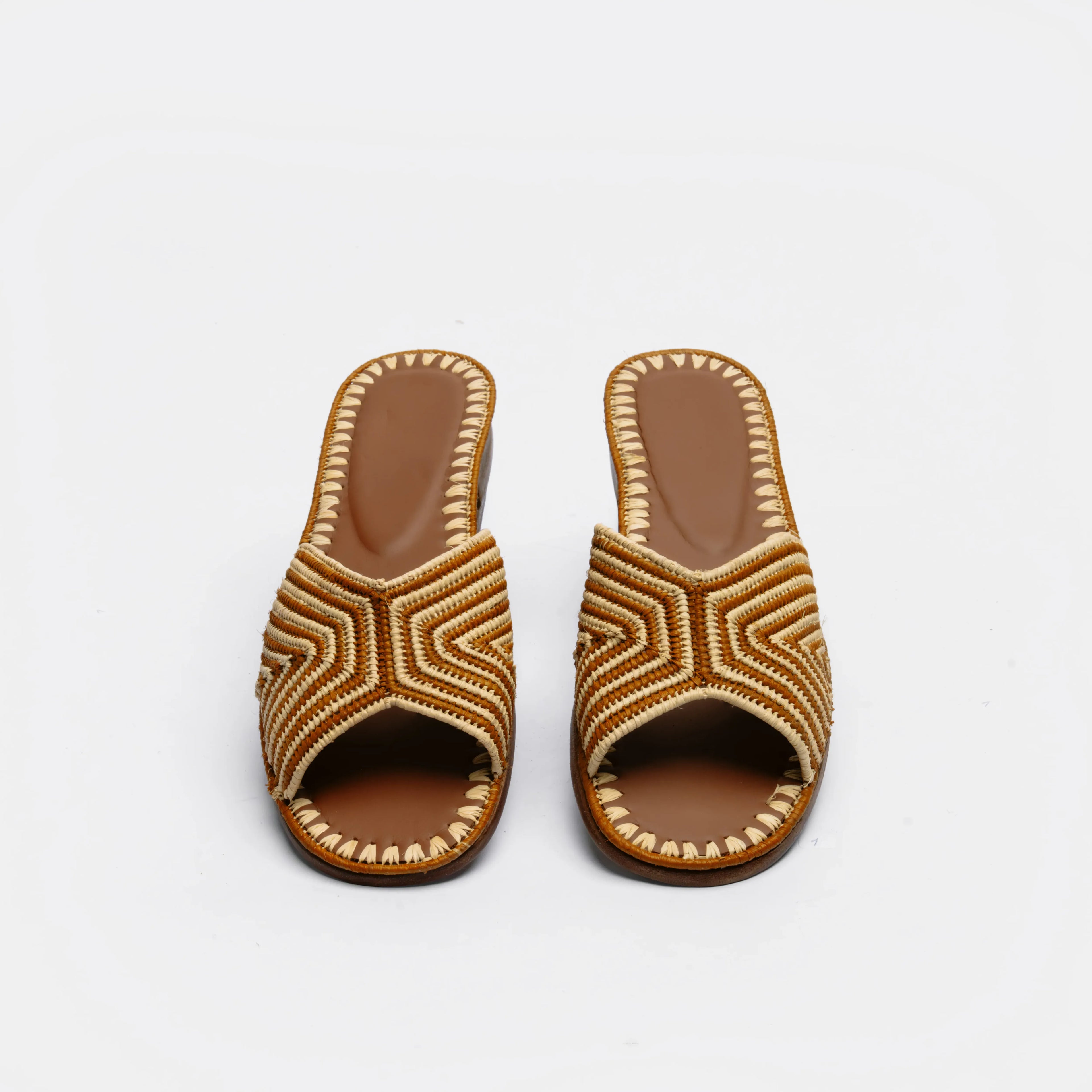A pair of women's open-toe slide sandals with geometric braided straps in brown and beige, set against a plain white background.