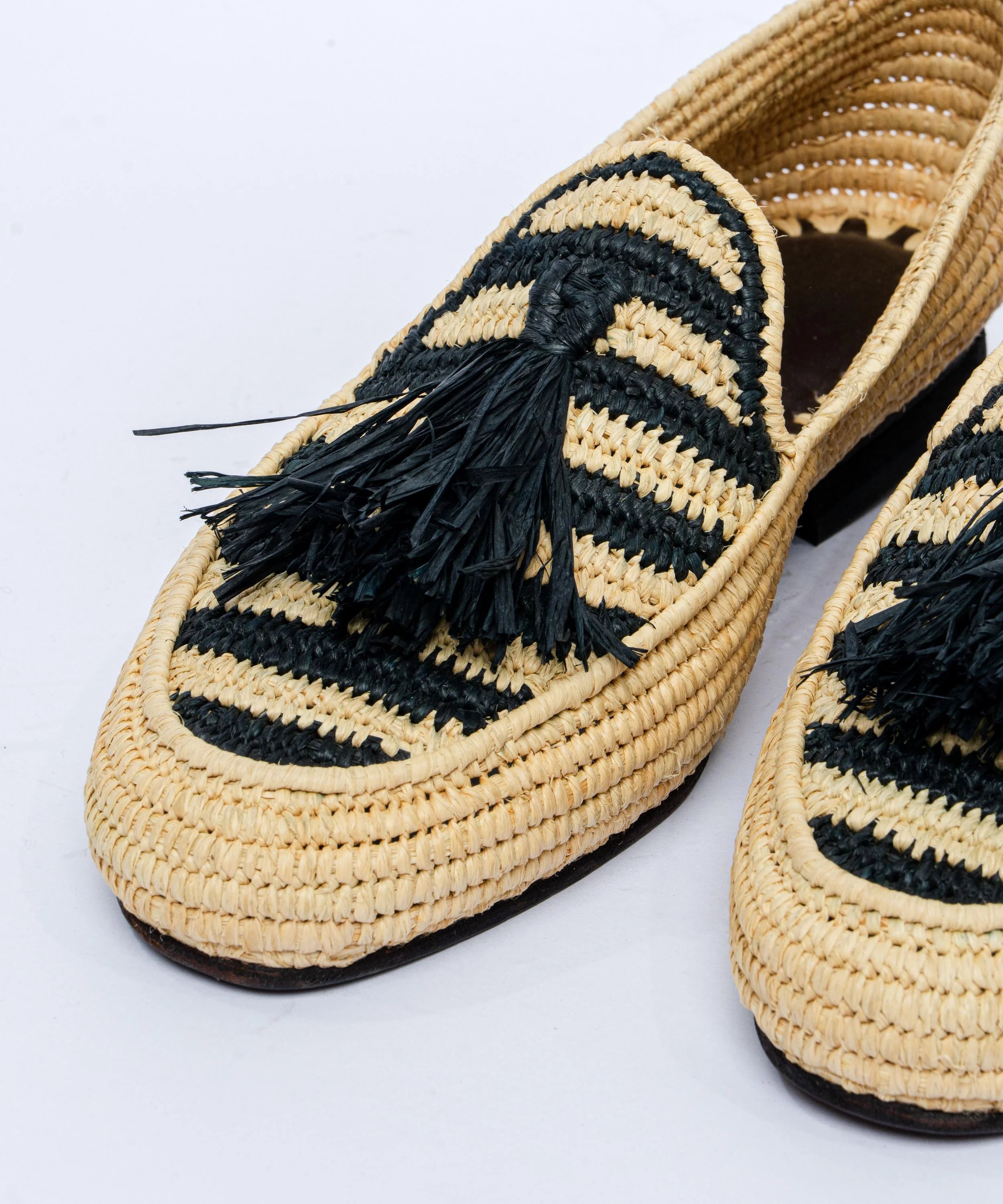 Woven shoes with black tassels on a light gray background